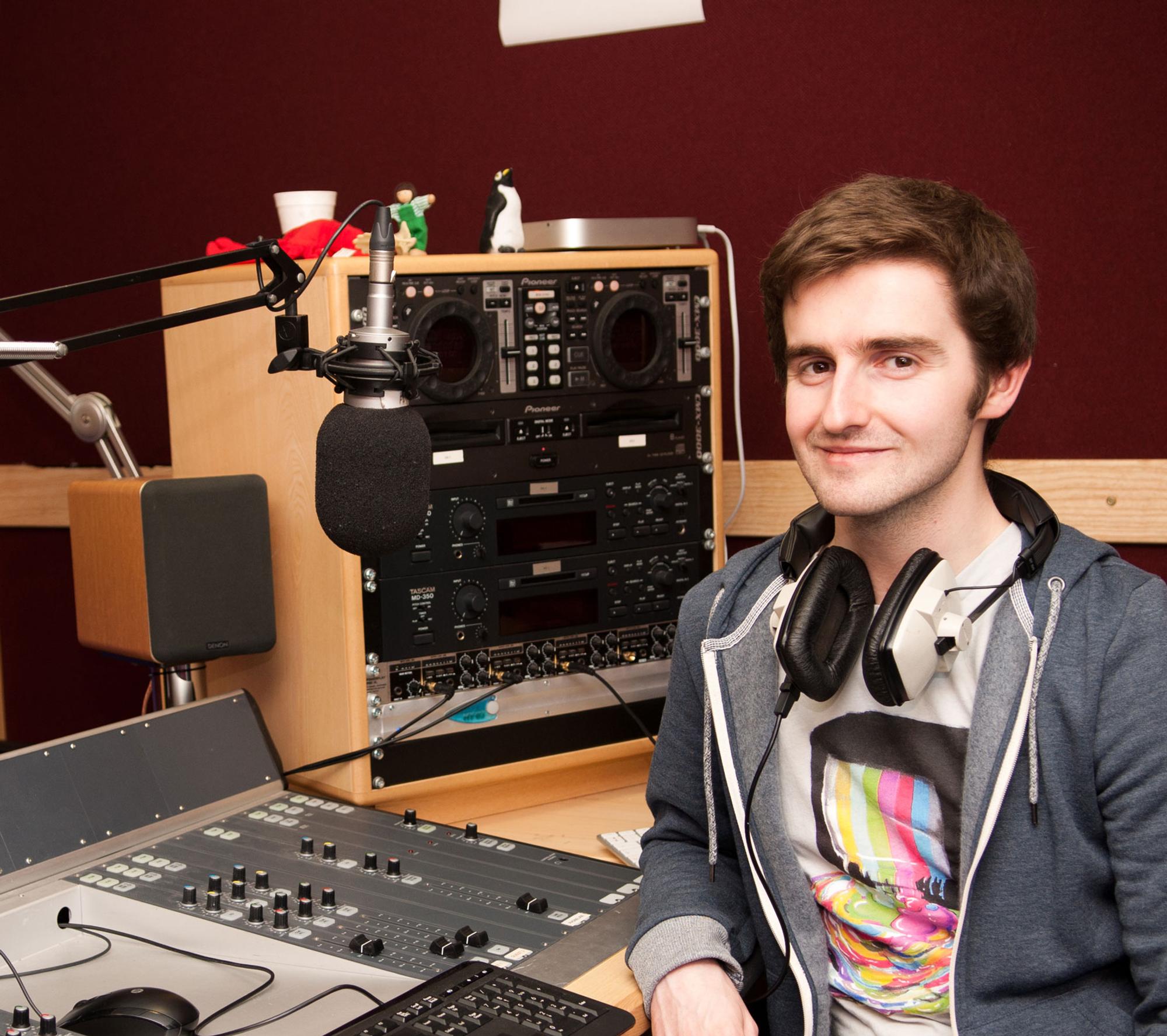 Male student wearing headphones sitting in front of a music mixer device
