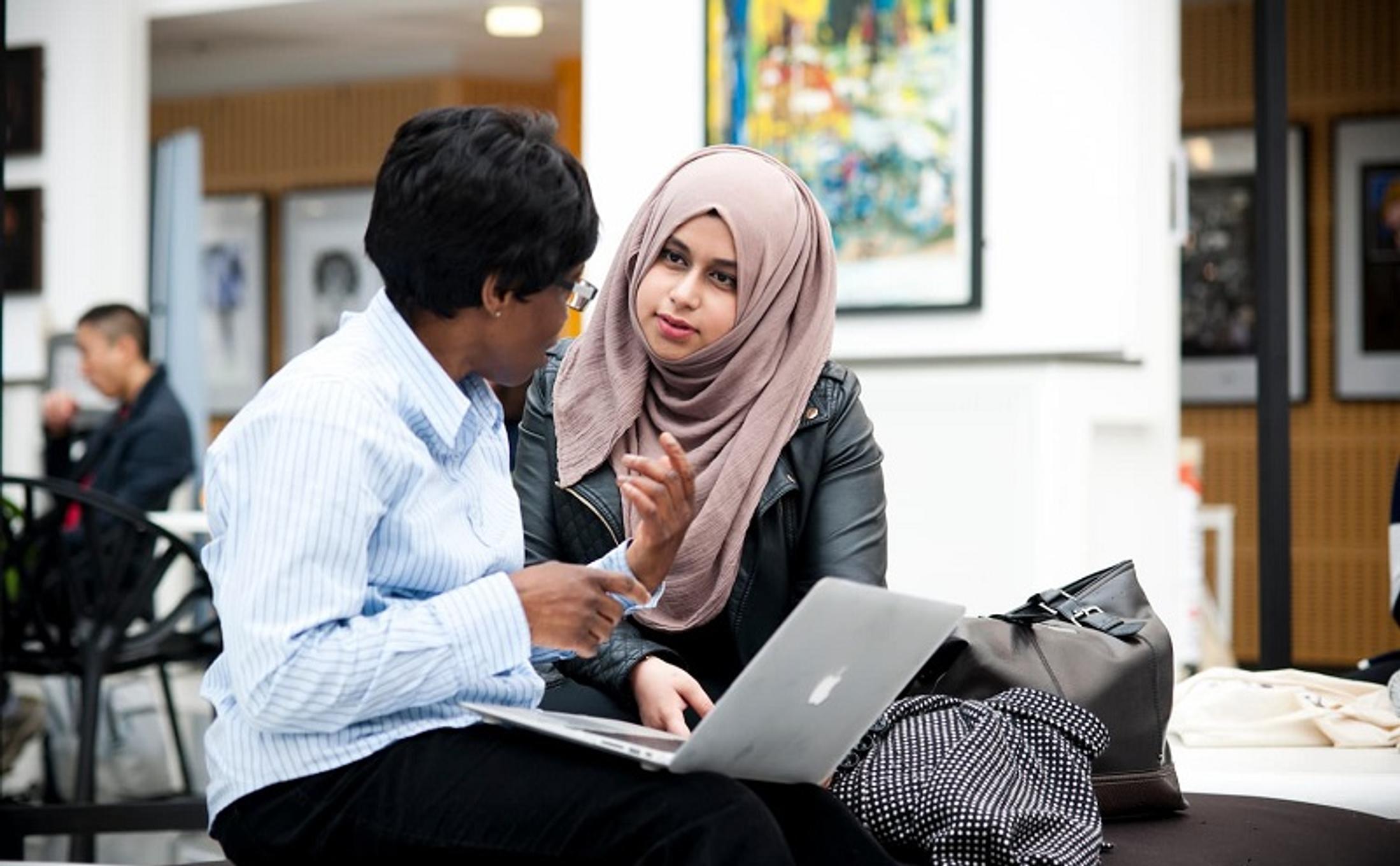 Two women sitting on a couch, engrossed in their laptops, working together in a comfortable setting.