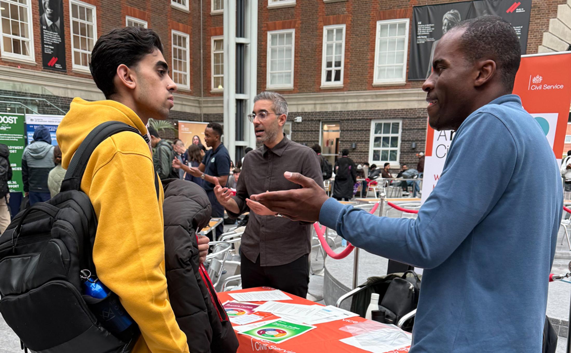 Two men in discussion in a busy building with a table between them