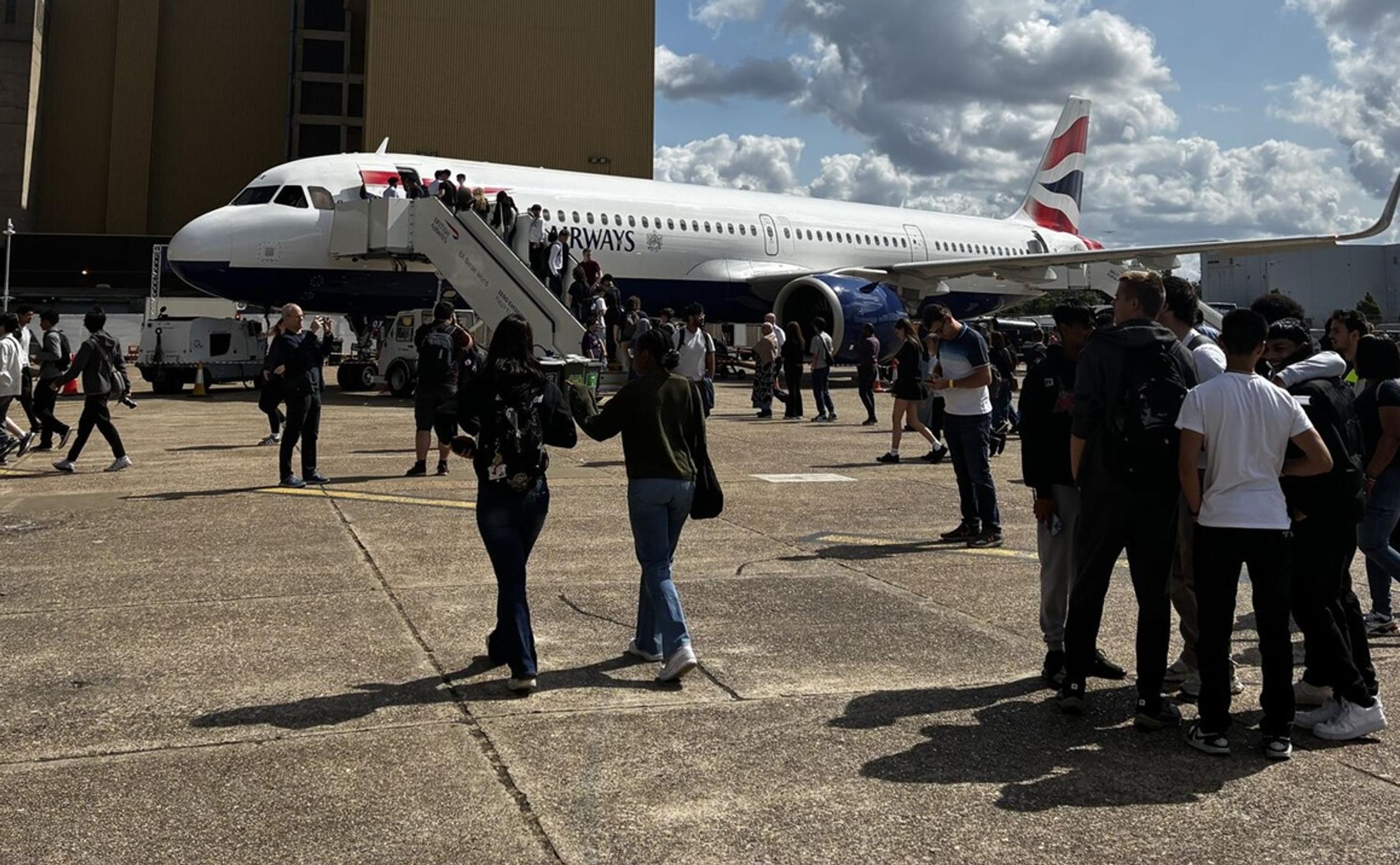Groups of people walking or standing in front of a BA plane at an airport