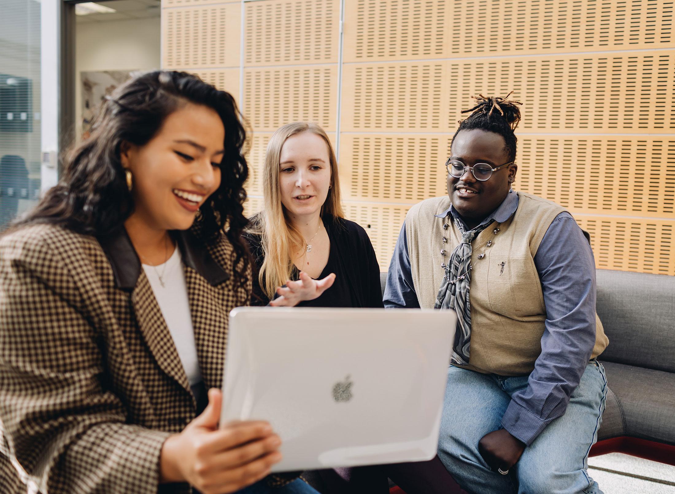 Three students in study area looking at laptop