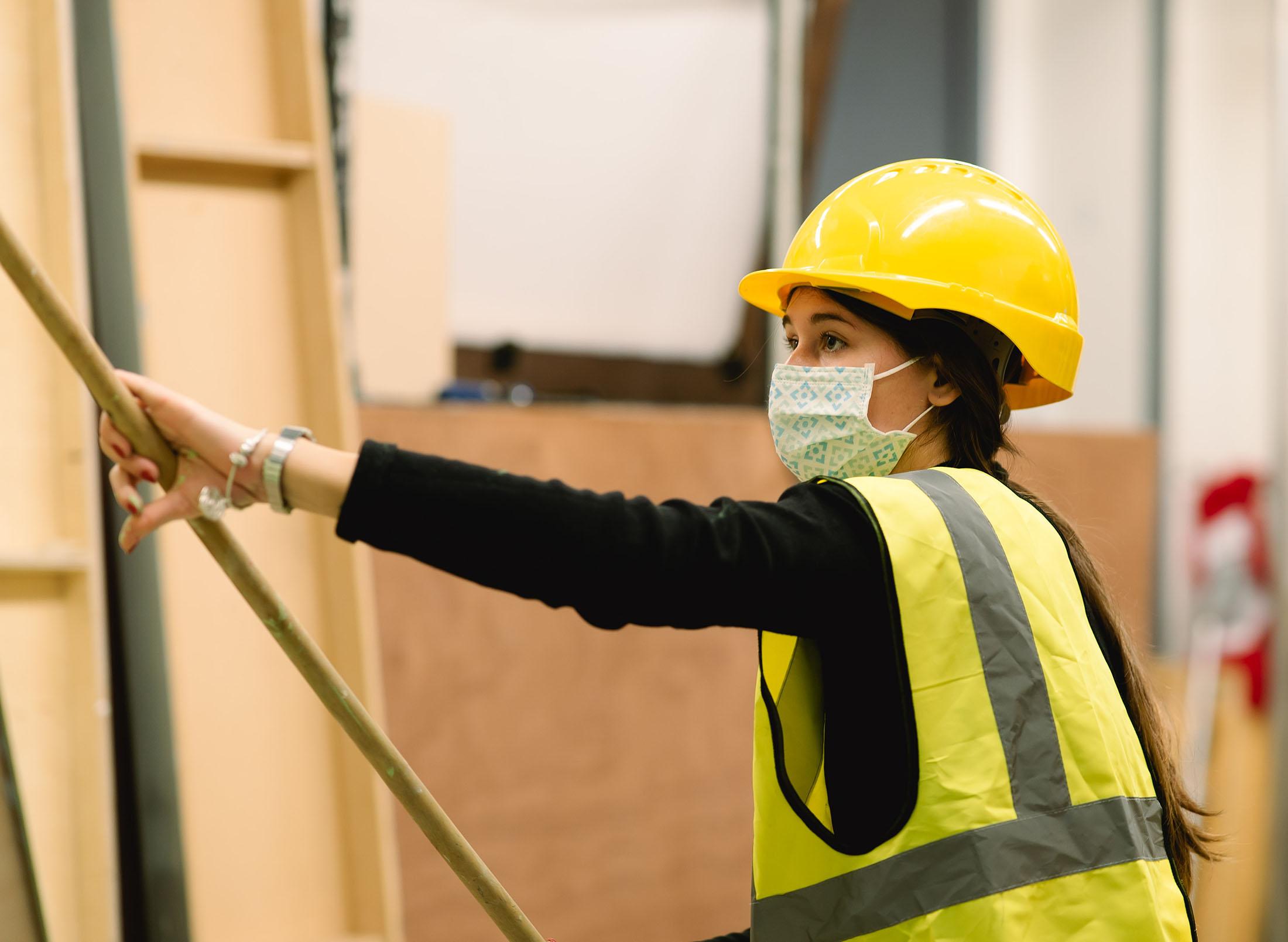Student with hardhat, facemask and hi-viz vest holding long stick