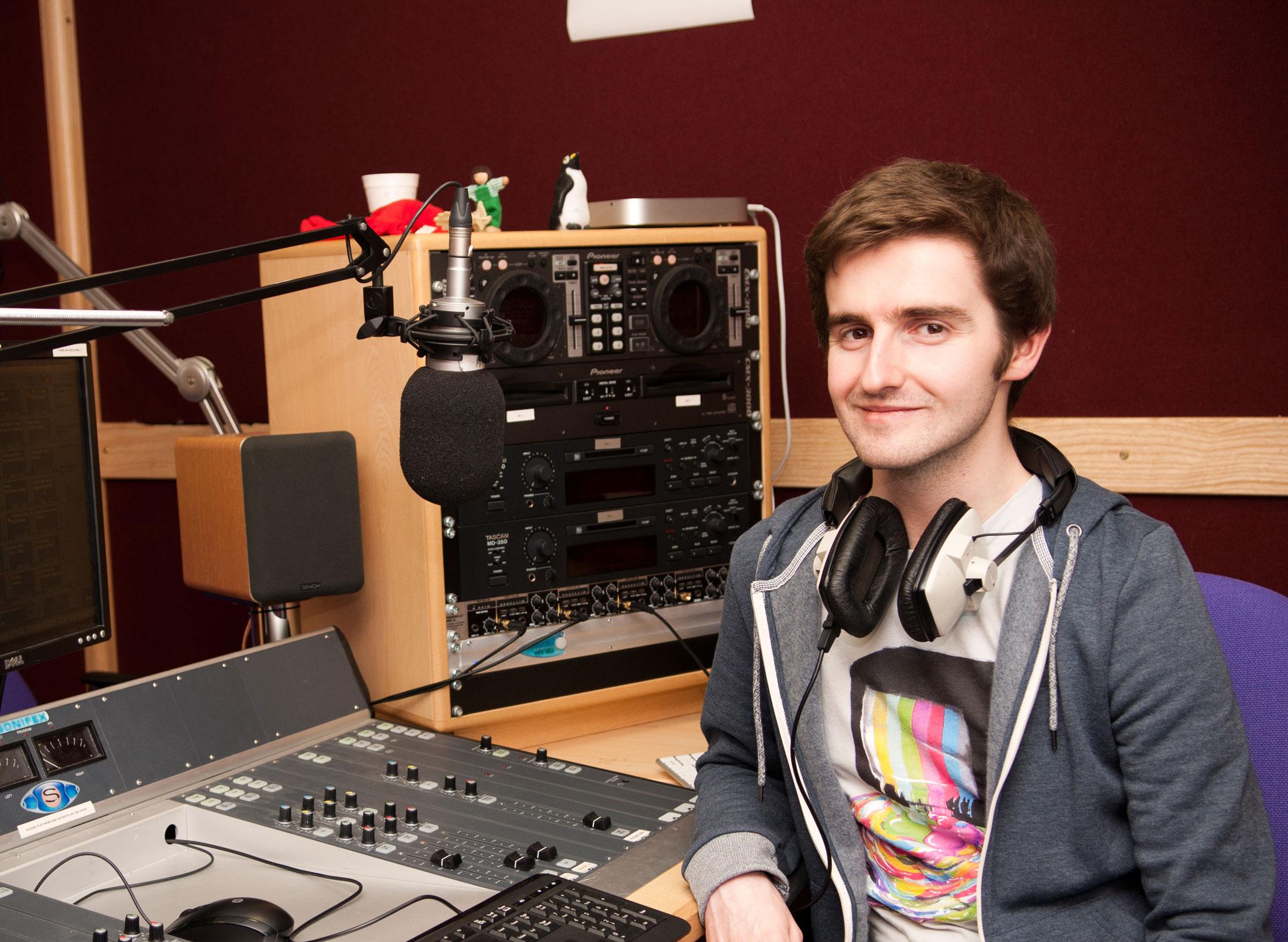 Male student wearing headphones sitting in front of a music mixer device