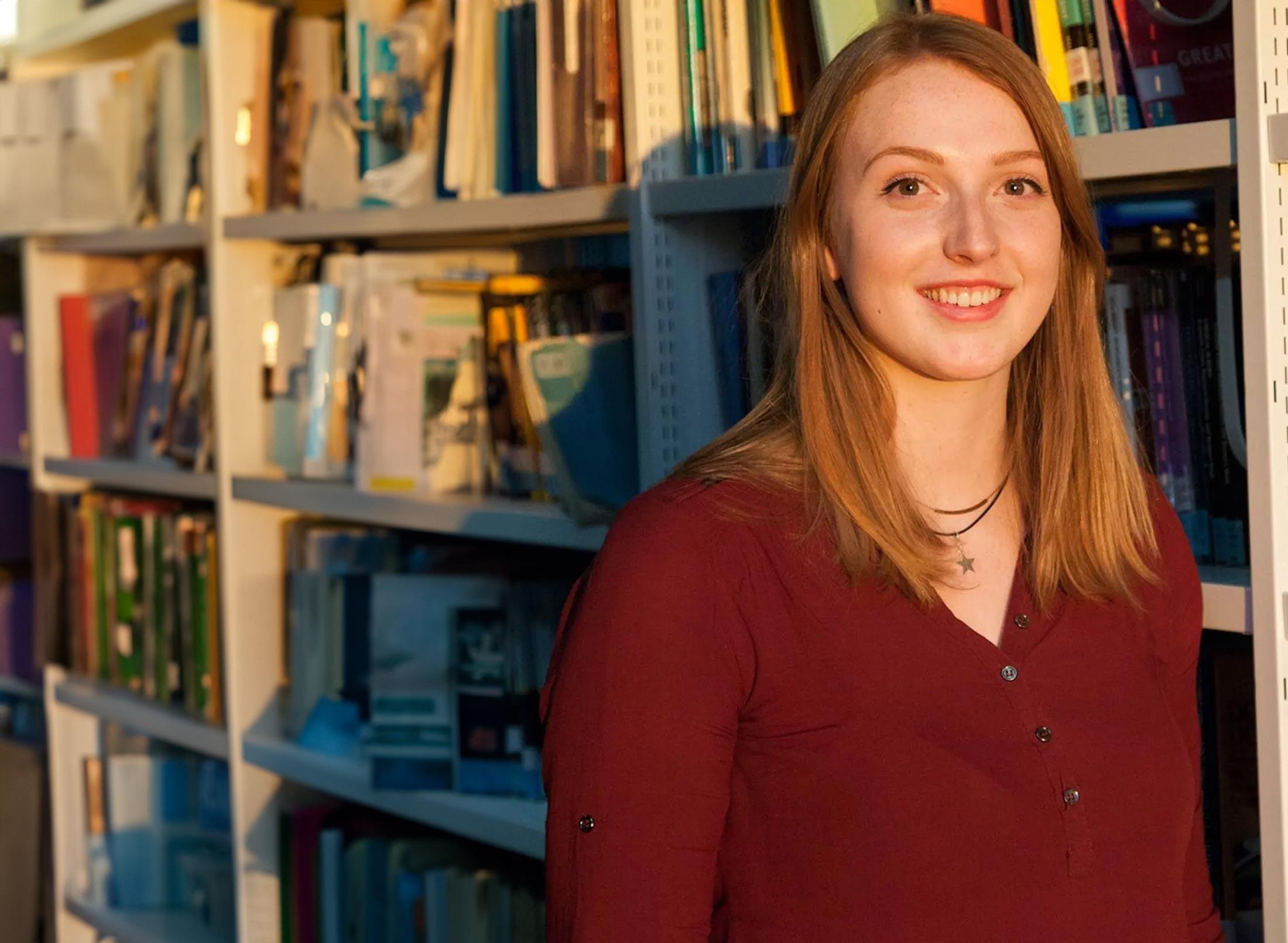 Female student stood in front of library shelf with books behind