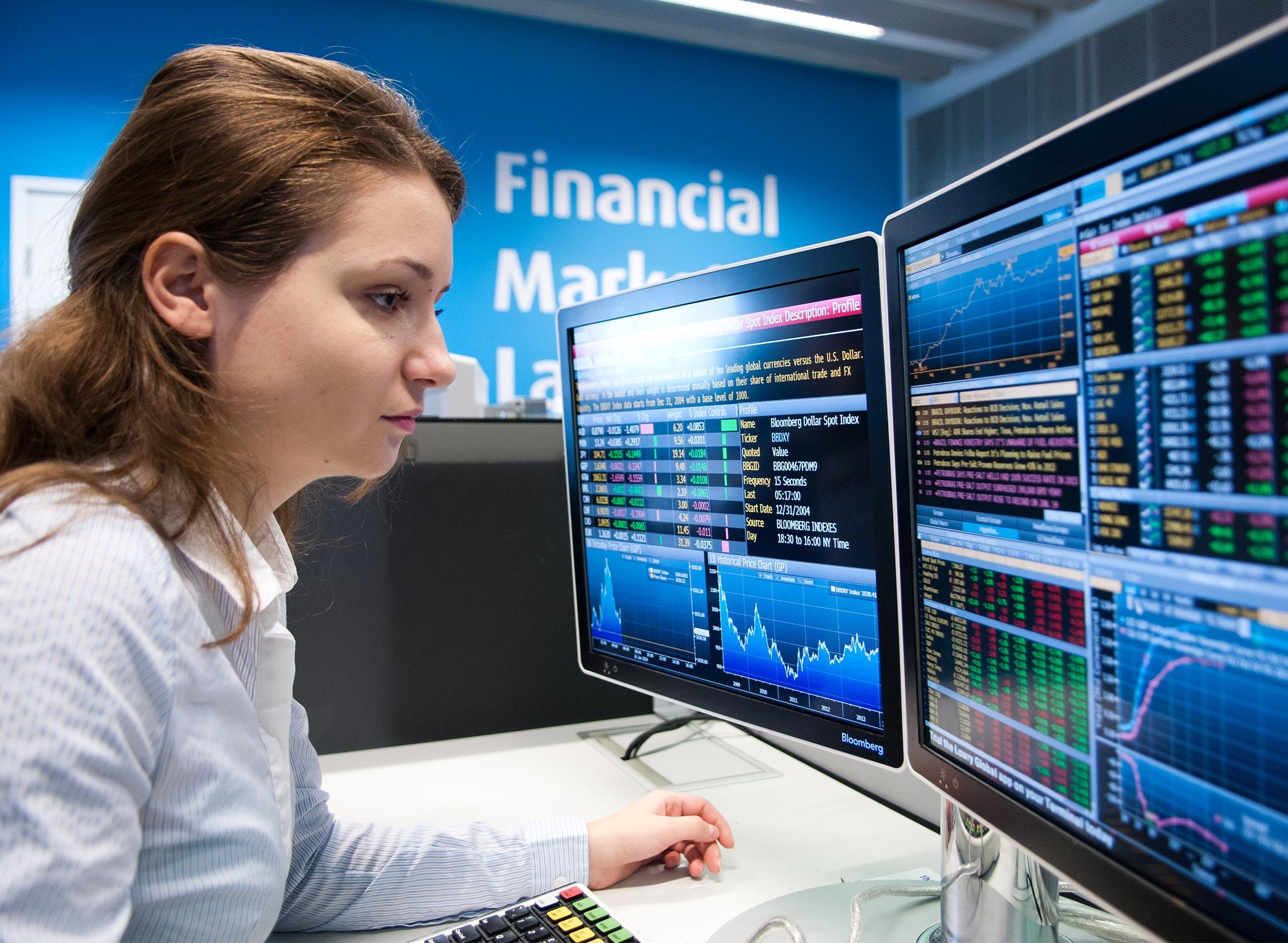 A female student sitting in front of a computer monitor displaying financial data in the Financial Markets Lab