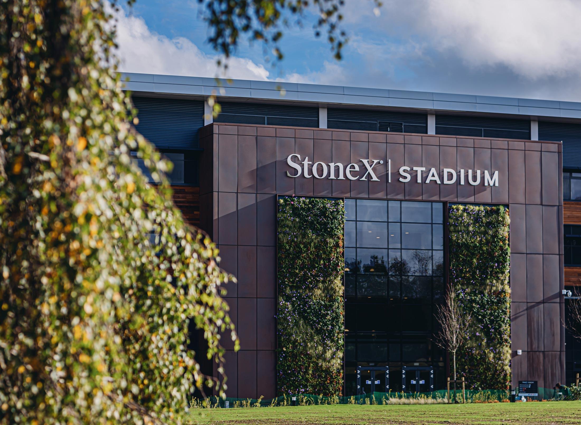 Large stadium exterior with grass and trees, stadium entrance says: Stone X Stadium