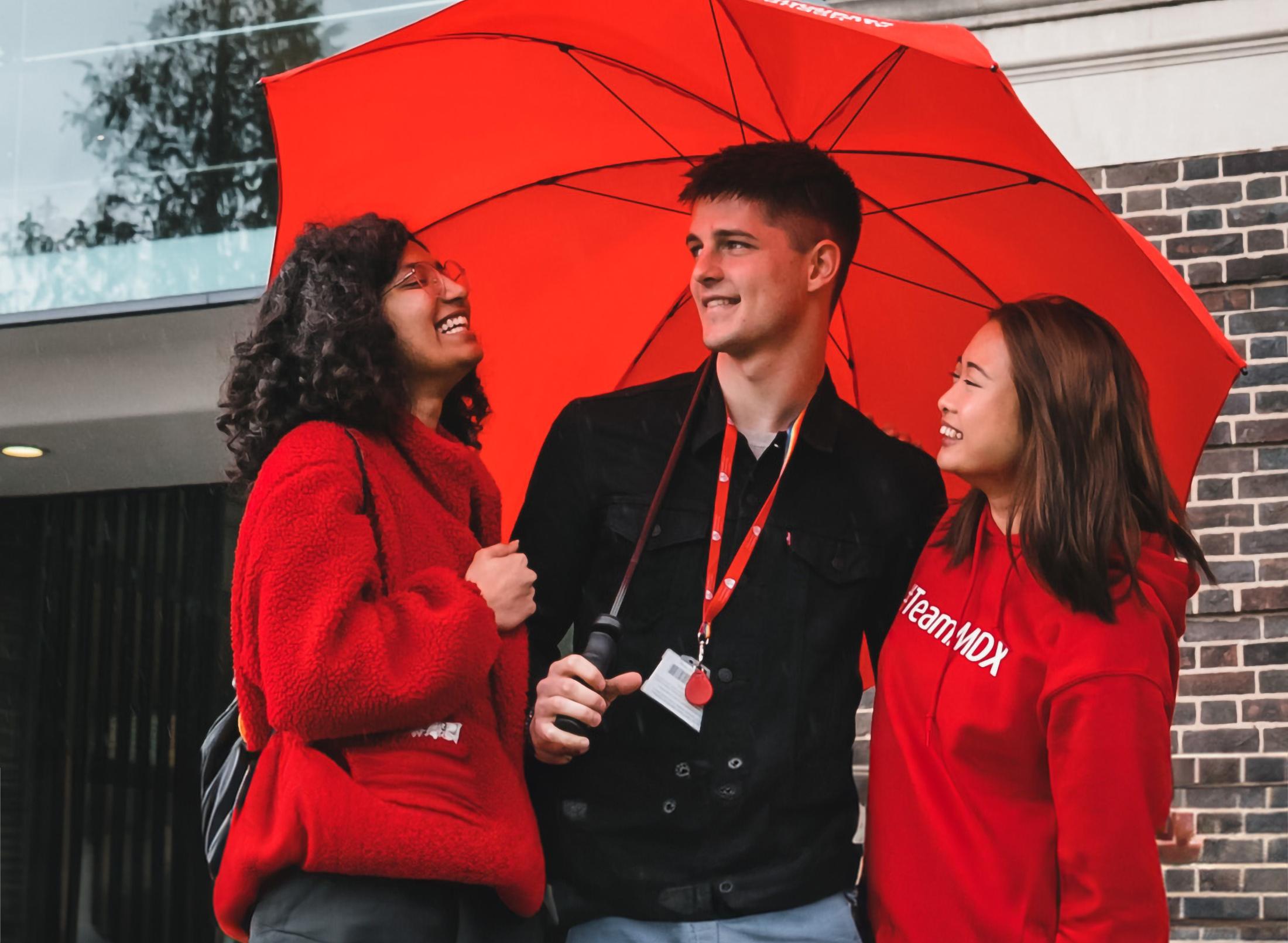 three happy students stand under an umbrella