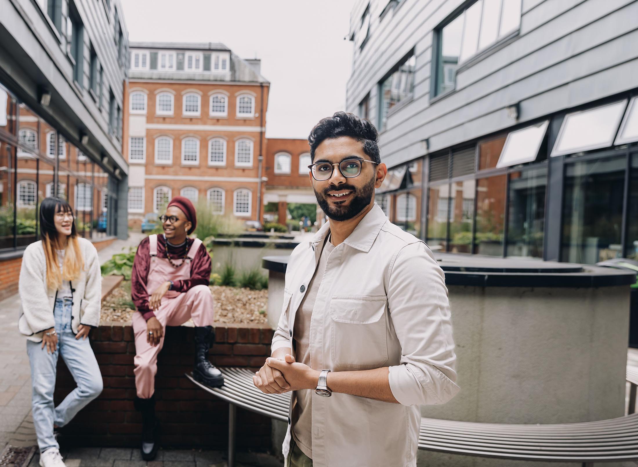 Student poses for picture while two others chat behind him