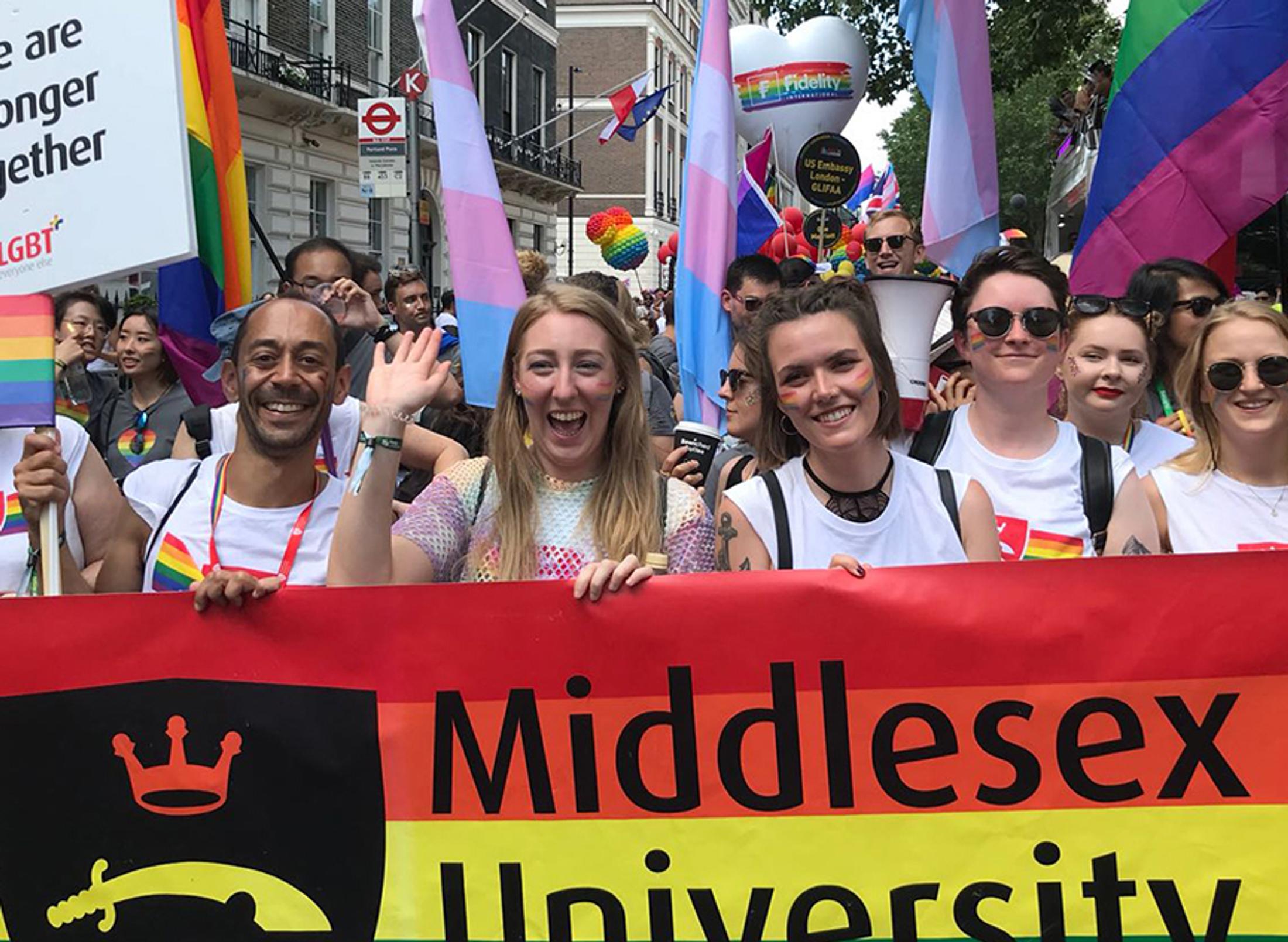 A diverse group of individuals proudly holding a rainbow flag, symbolizing unity, inclusivity, and support for the LGBTQ+ community.