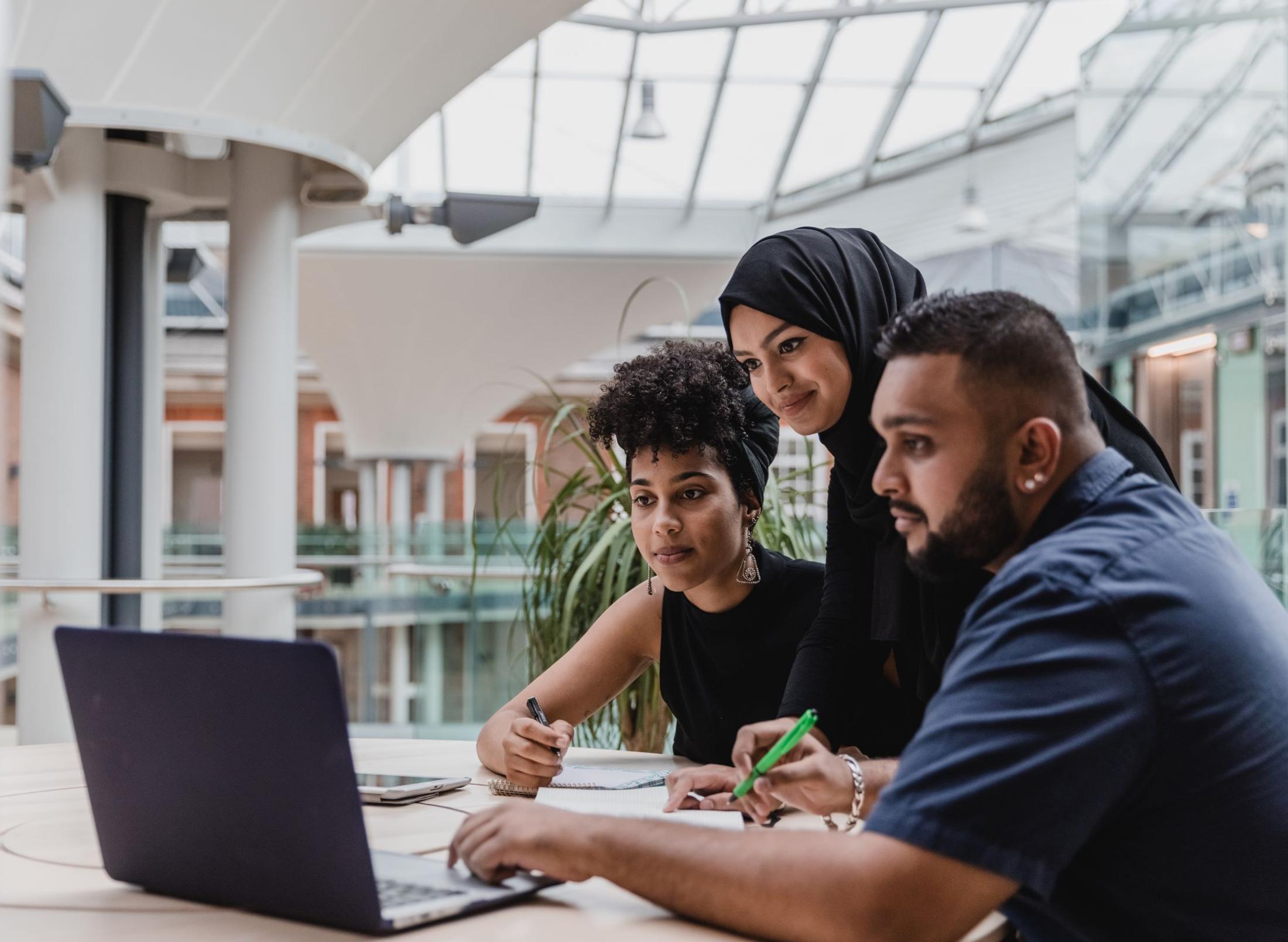 3 students looking at a laptop seated at a table in the quad