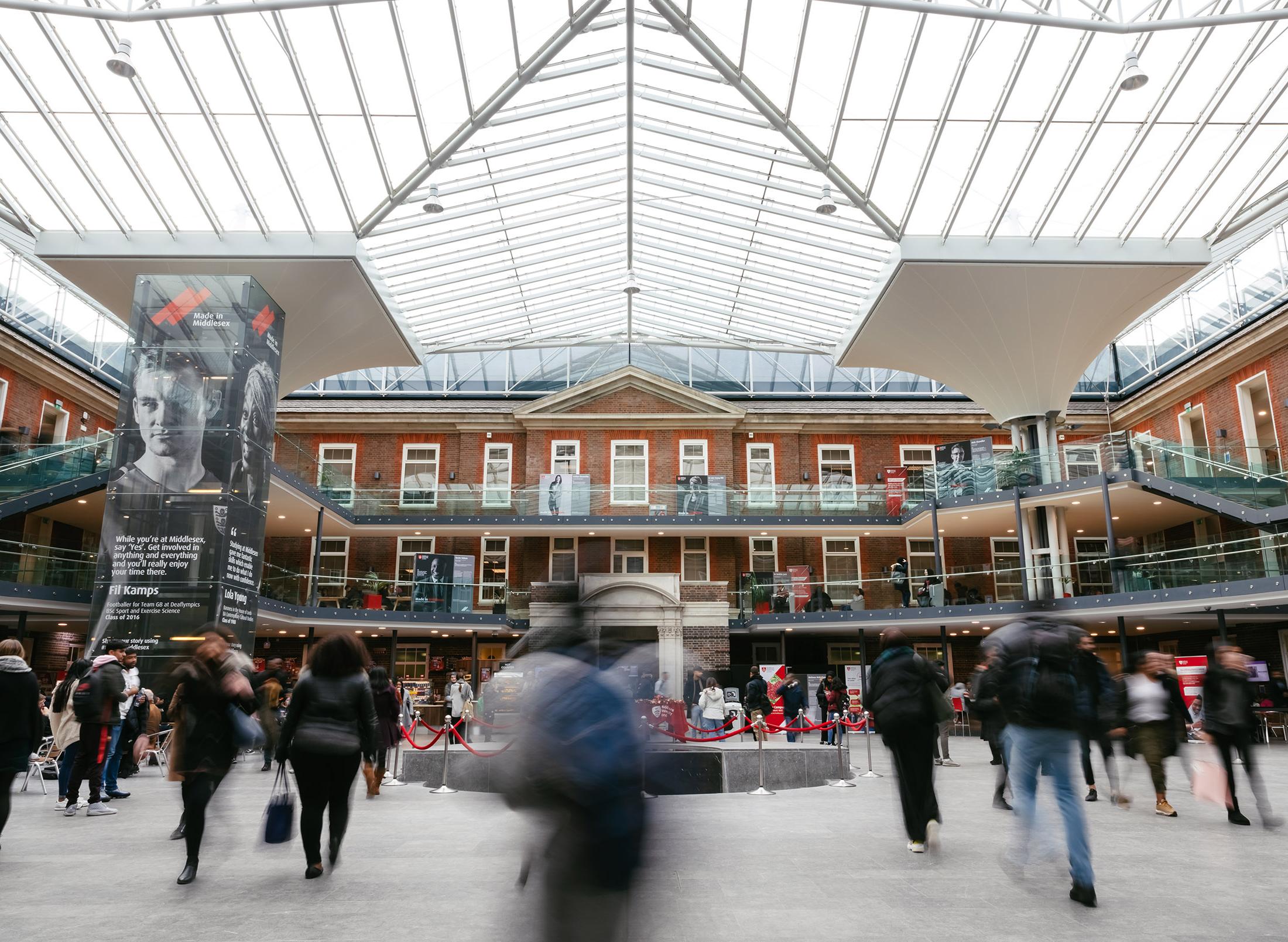 Inside of college building, busy quad with transparent roof, blurred motion as people move around