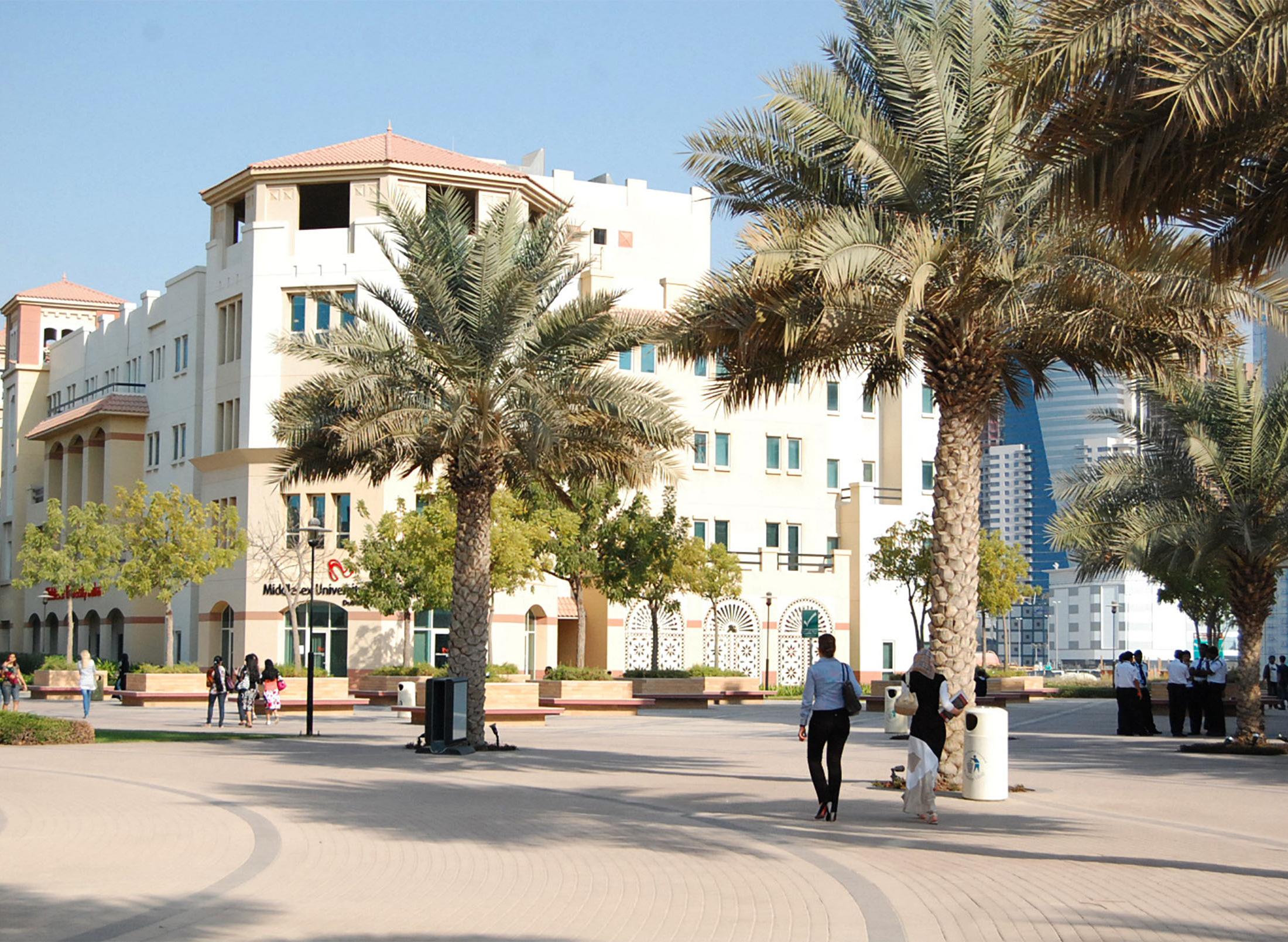 students walking along a street with dubai campus and palm trees in the background