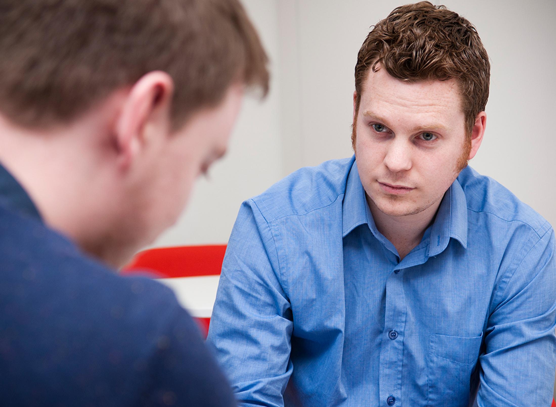 student sat in blue shirt sat down facing another man