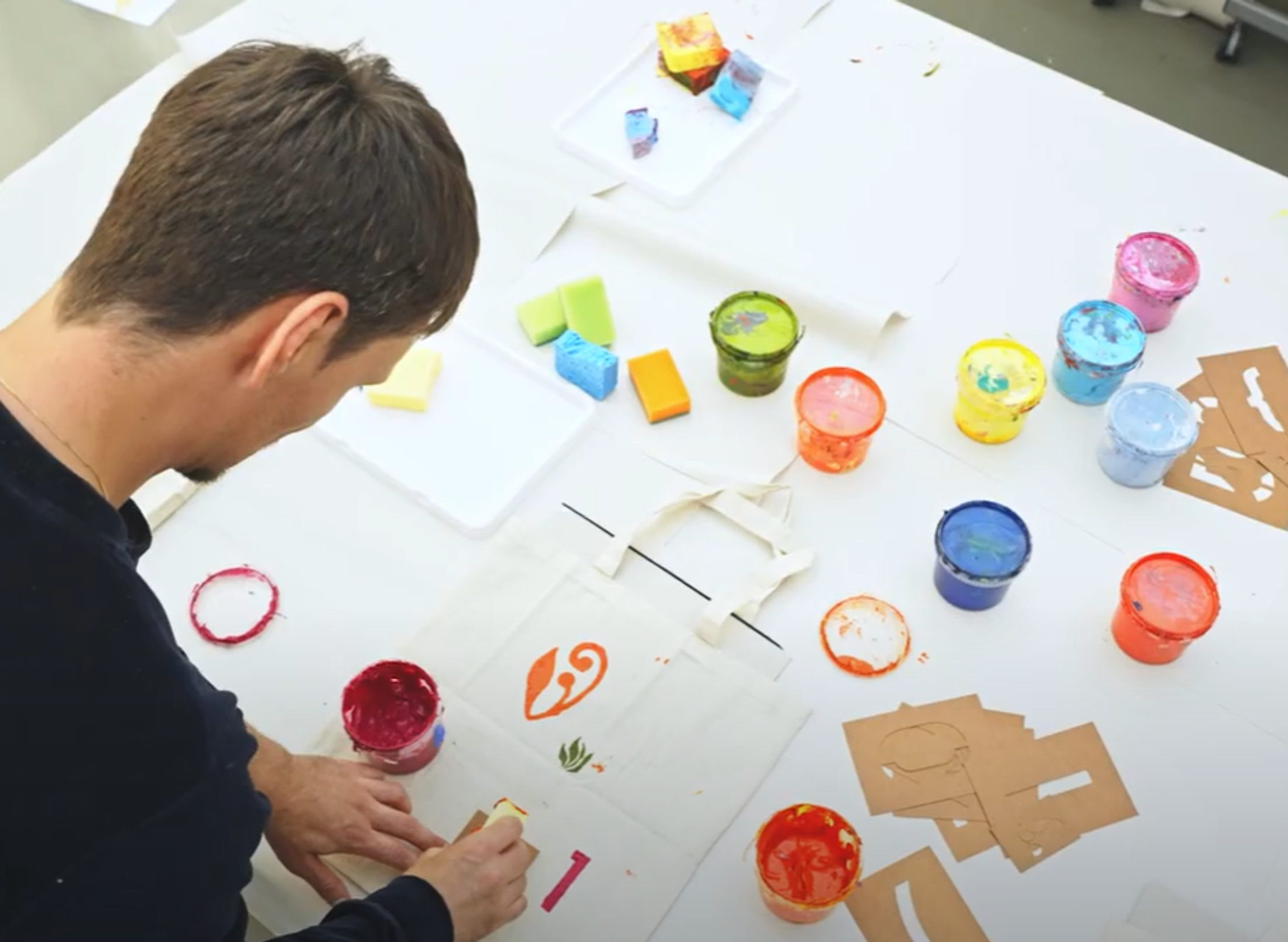 Student working on a white canvas with coloured paint pots on a table
