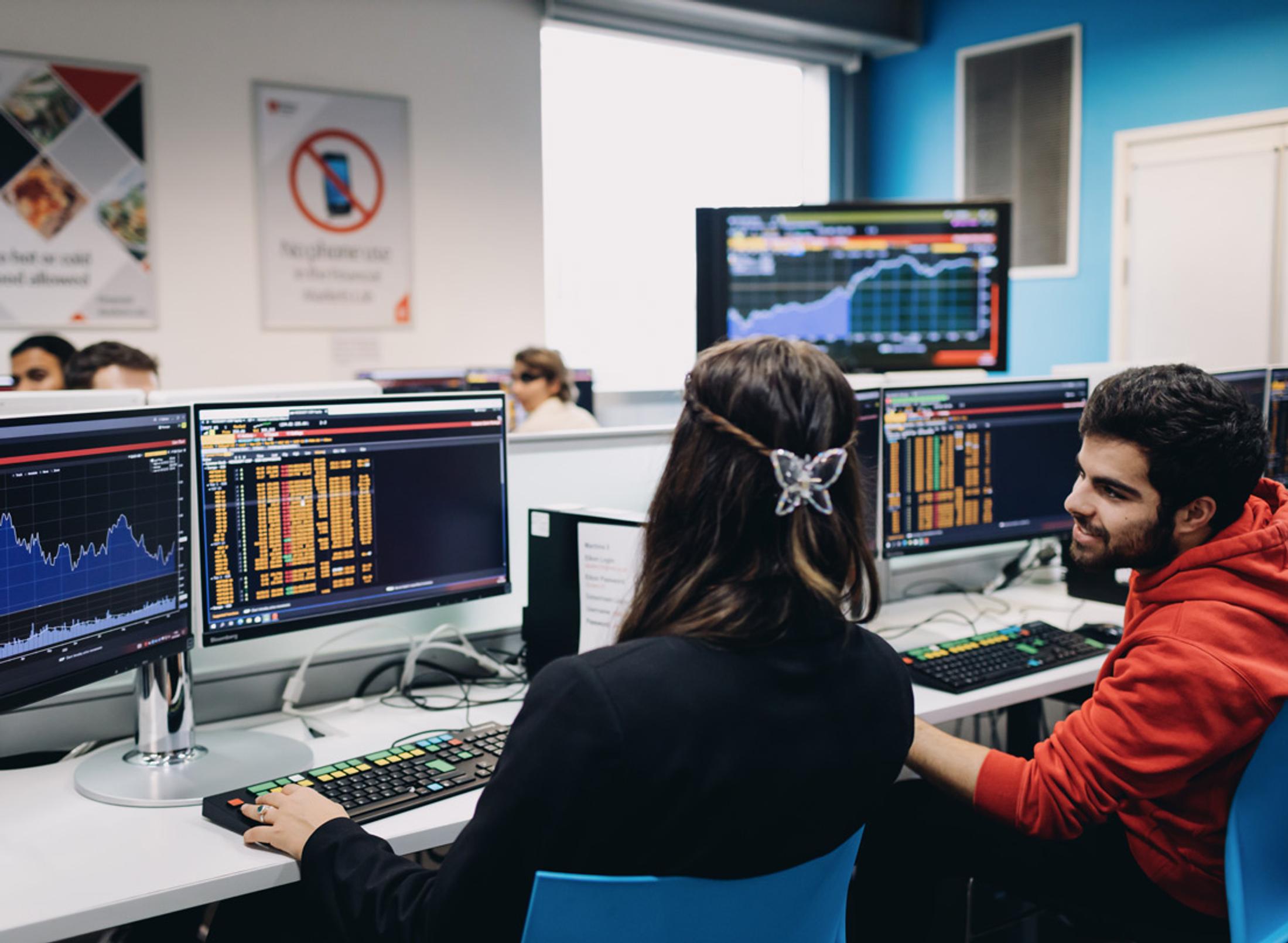 Two young people looking at financial forecasts on computer monitors