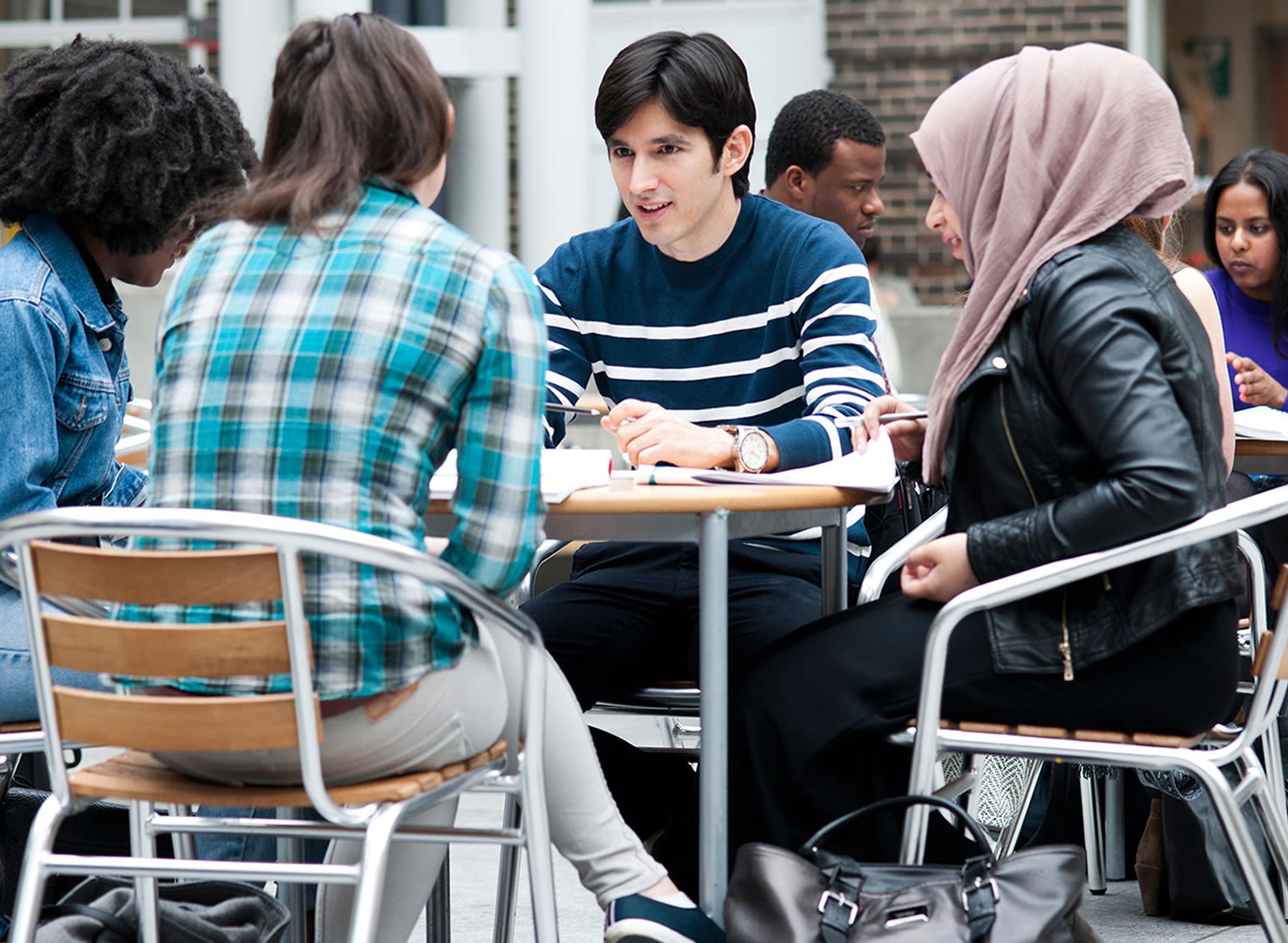 Four students sitting around a table at the Mdx Uni quad, chatting