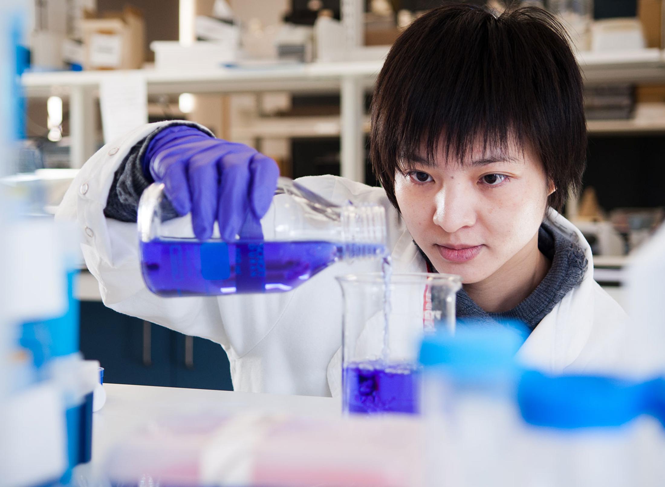 oriental student in a lab mixing chemicals