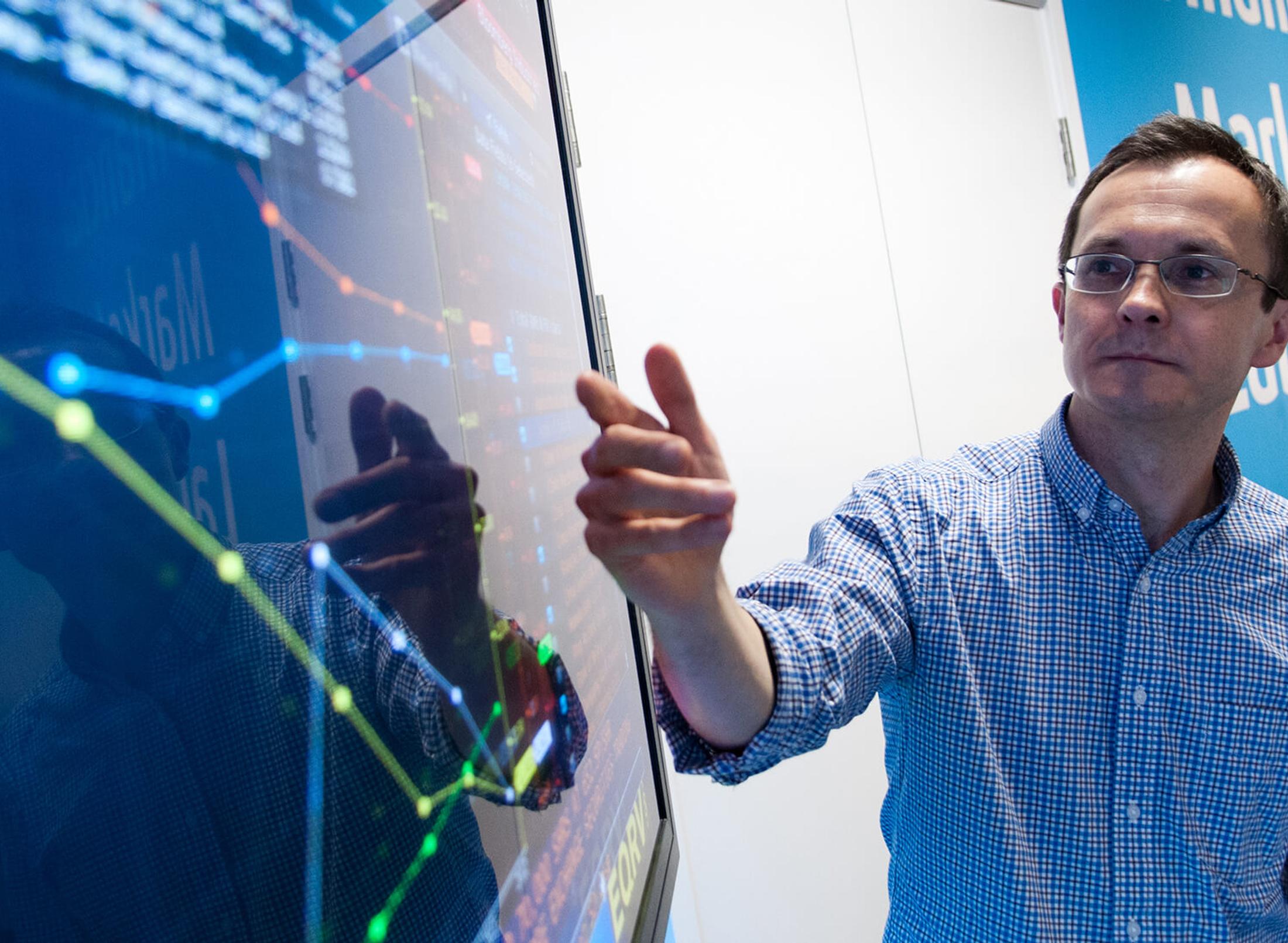 lecturer pointing to financial dashboard on large screen