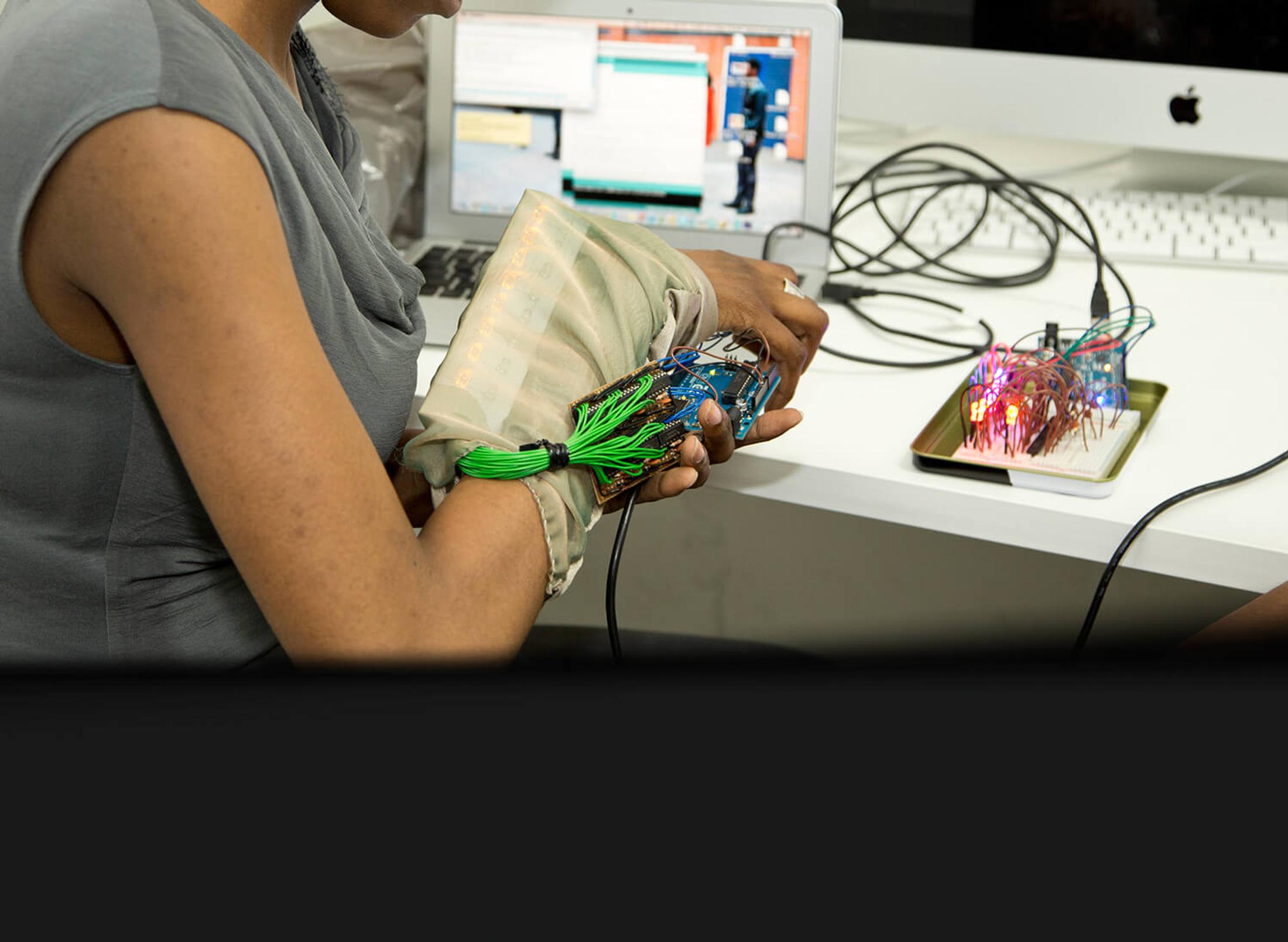 A student is sitting at a desk in front of a computer, working with electrical equipment