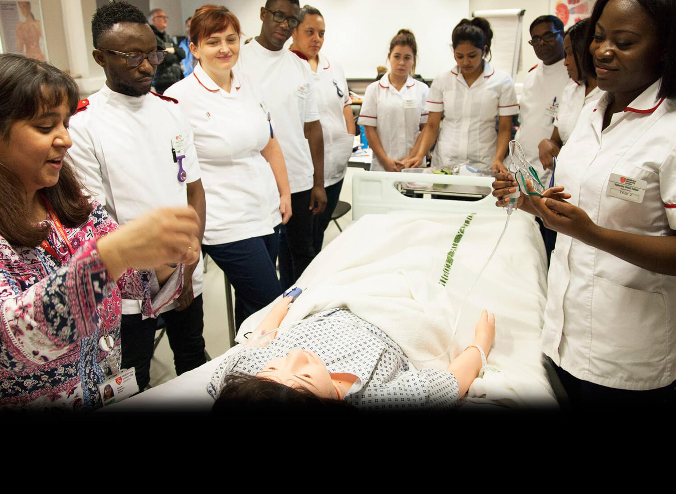 A group of female and male student nurses standing around a patient's bed, while a tutor is explaining the treatment to them
