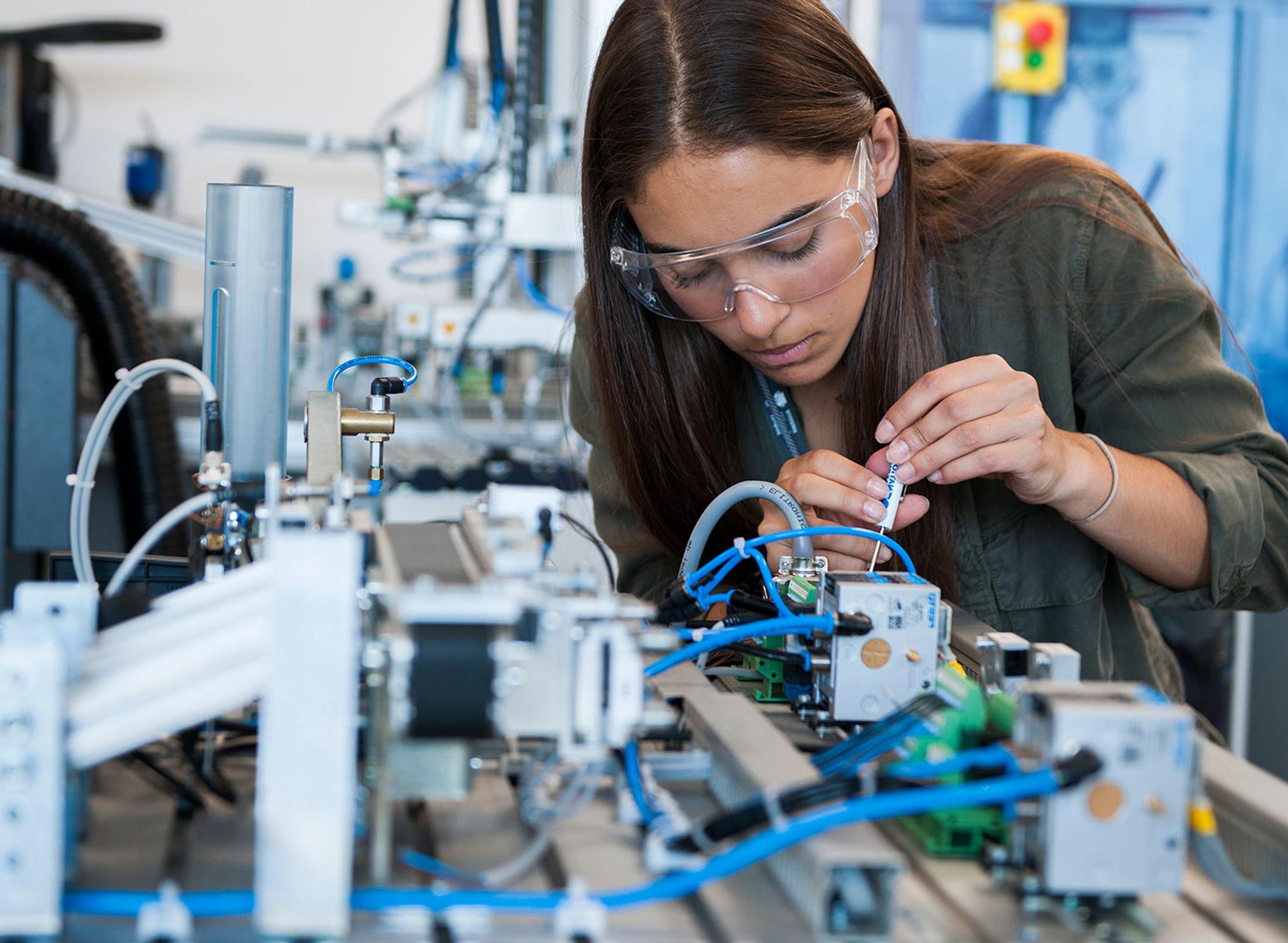 female student wearing googles works on circuitry with small screwdriver