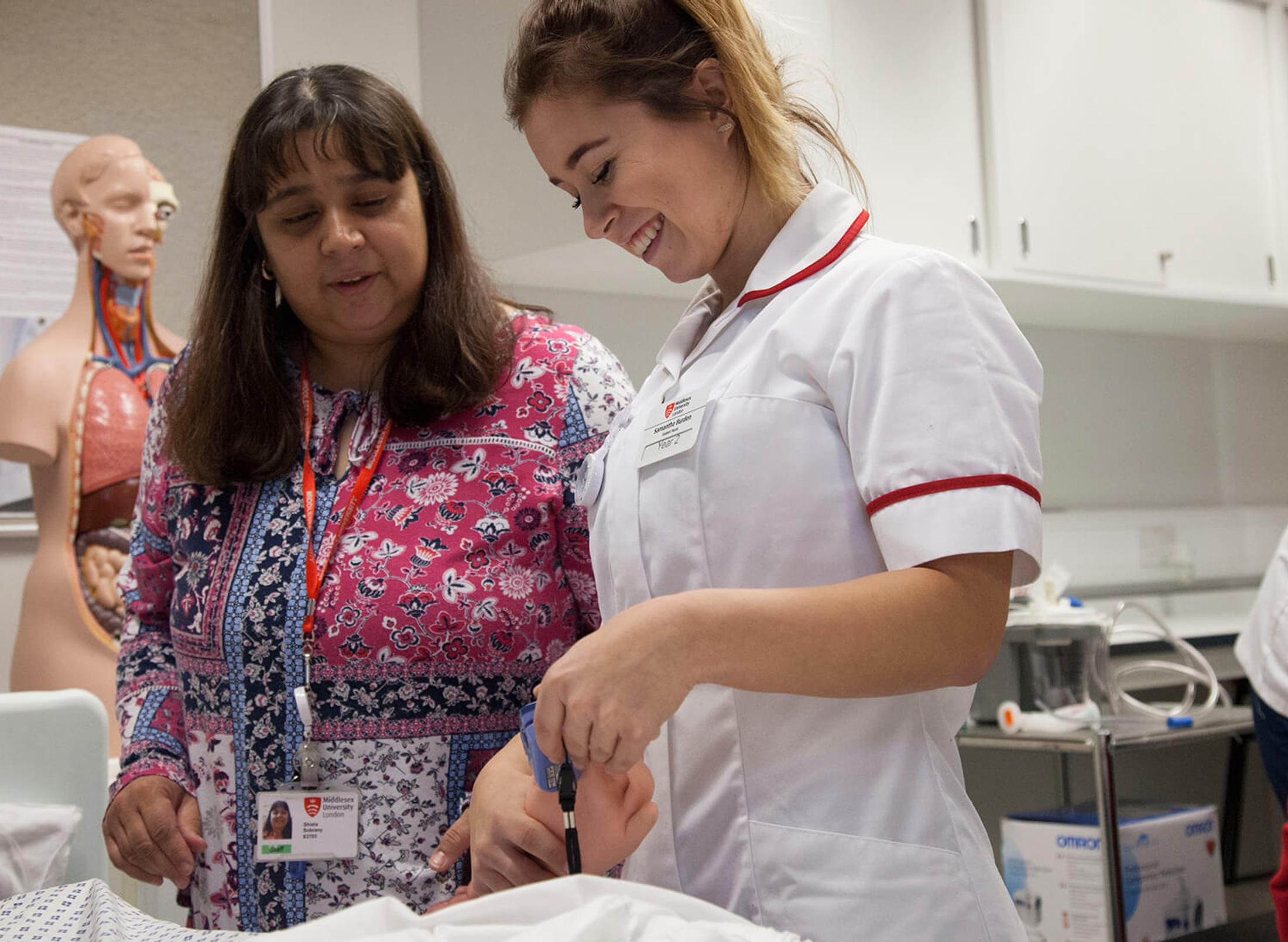 Two nurses assisting a baby in a hospital room.
