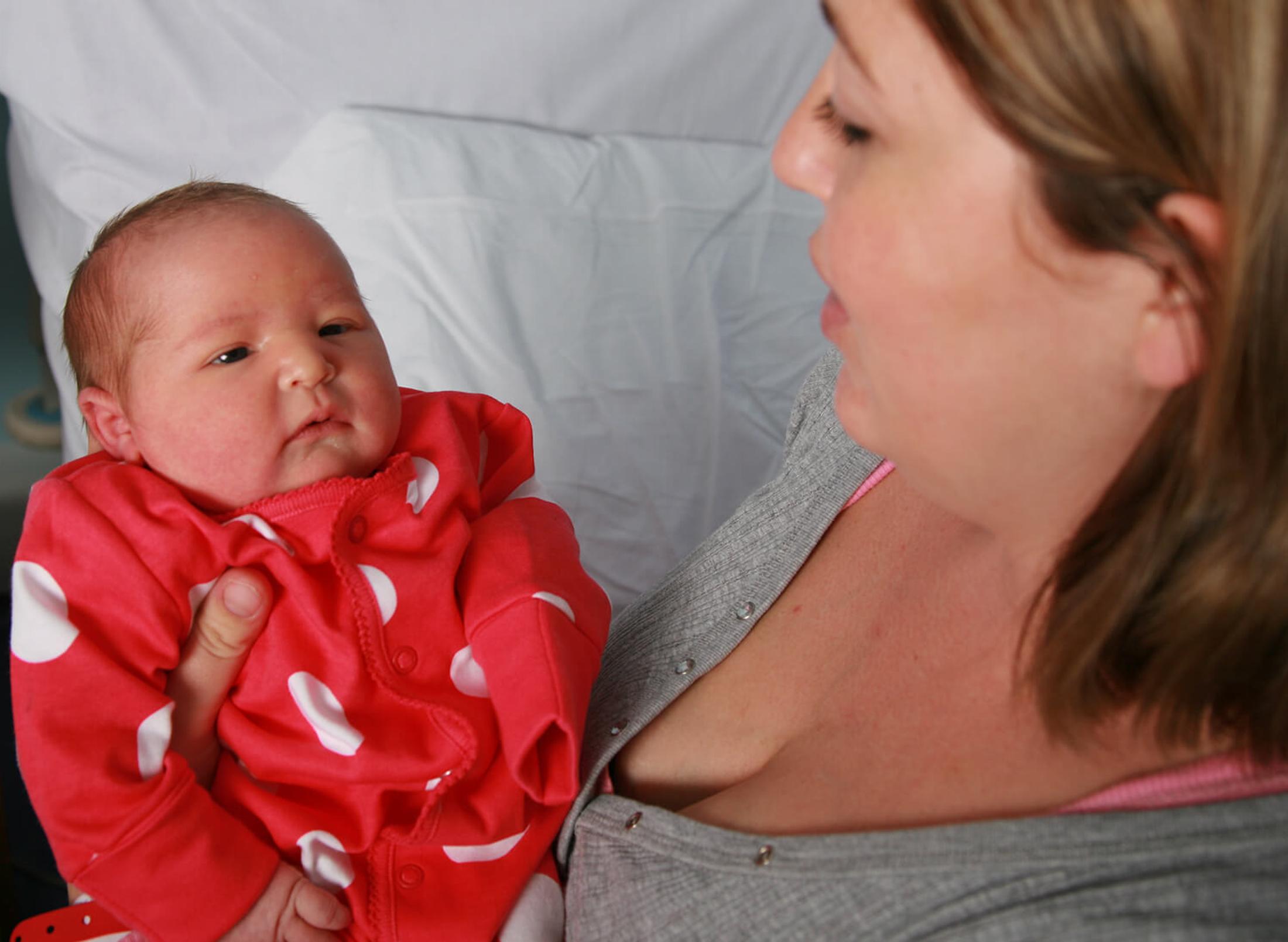 Mother holding baby in red spotted baby grow