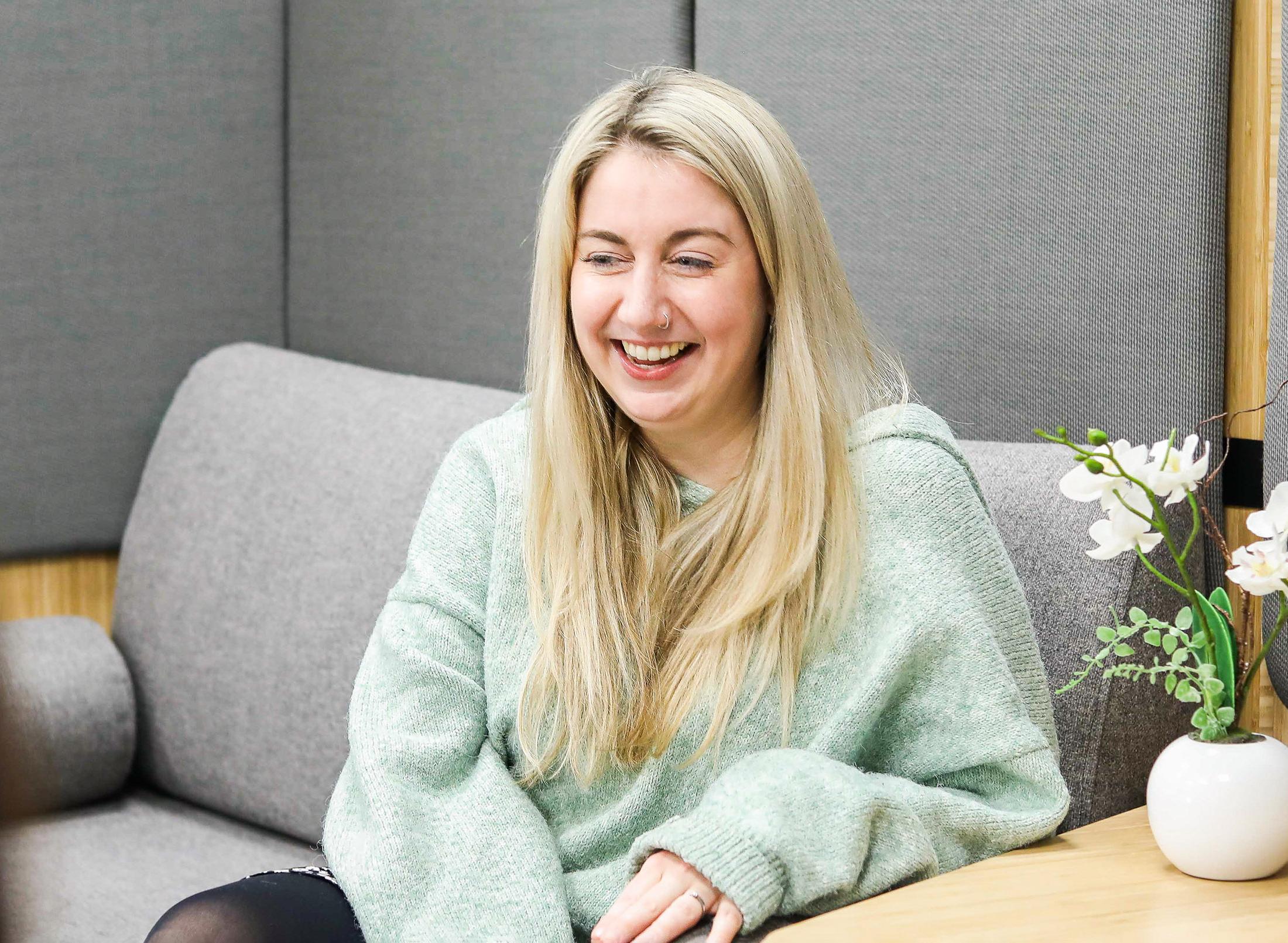 A happy student sitting on a sofa, appears to be listening to someone speaking