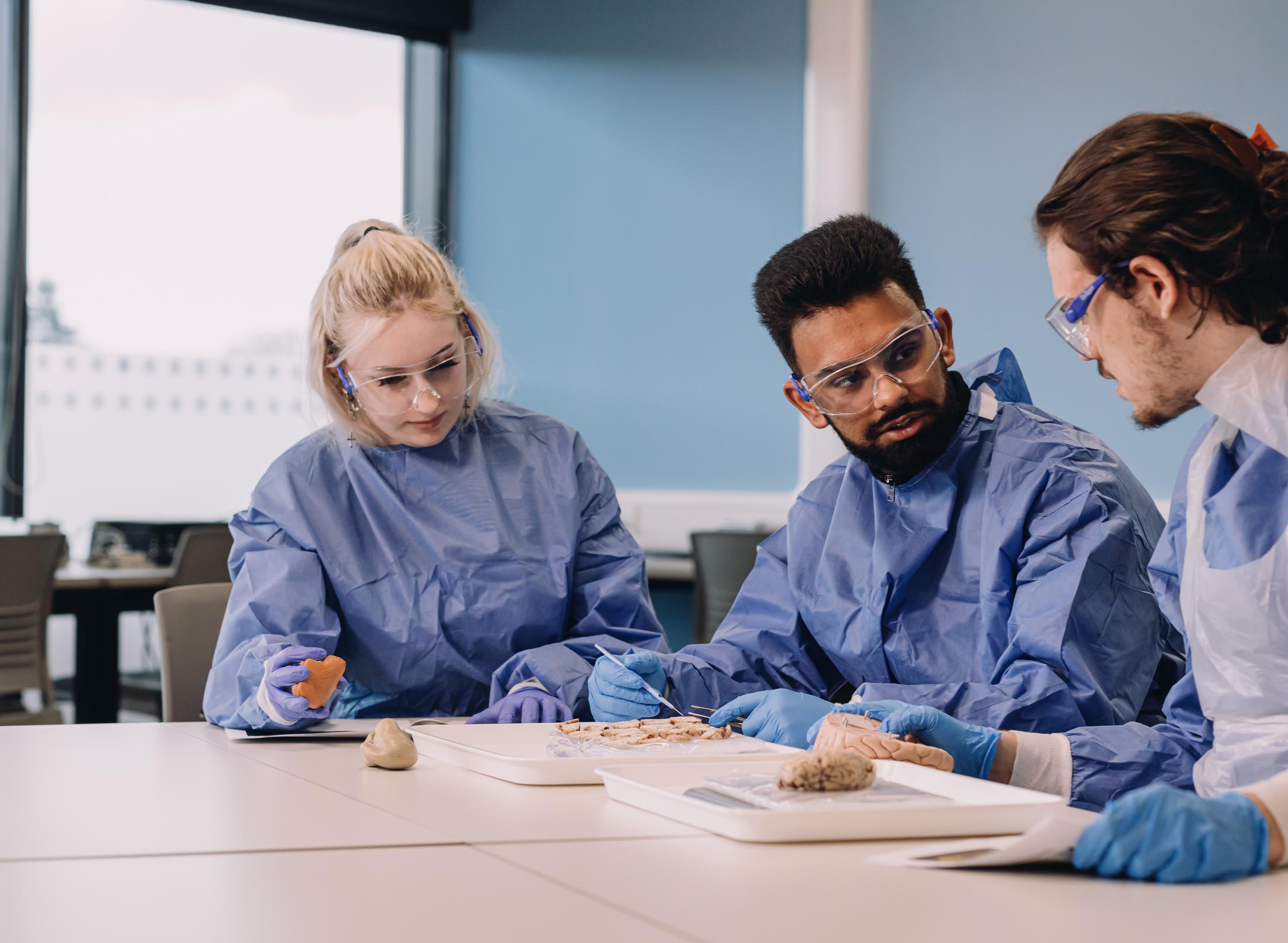 Three medical professionals in blue scrubs examining an object on a table.
