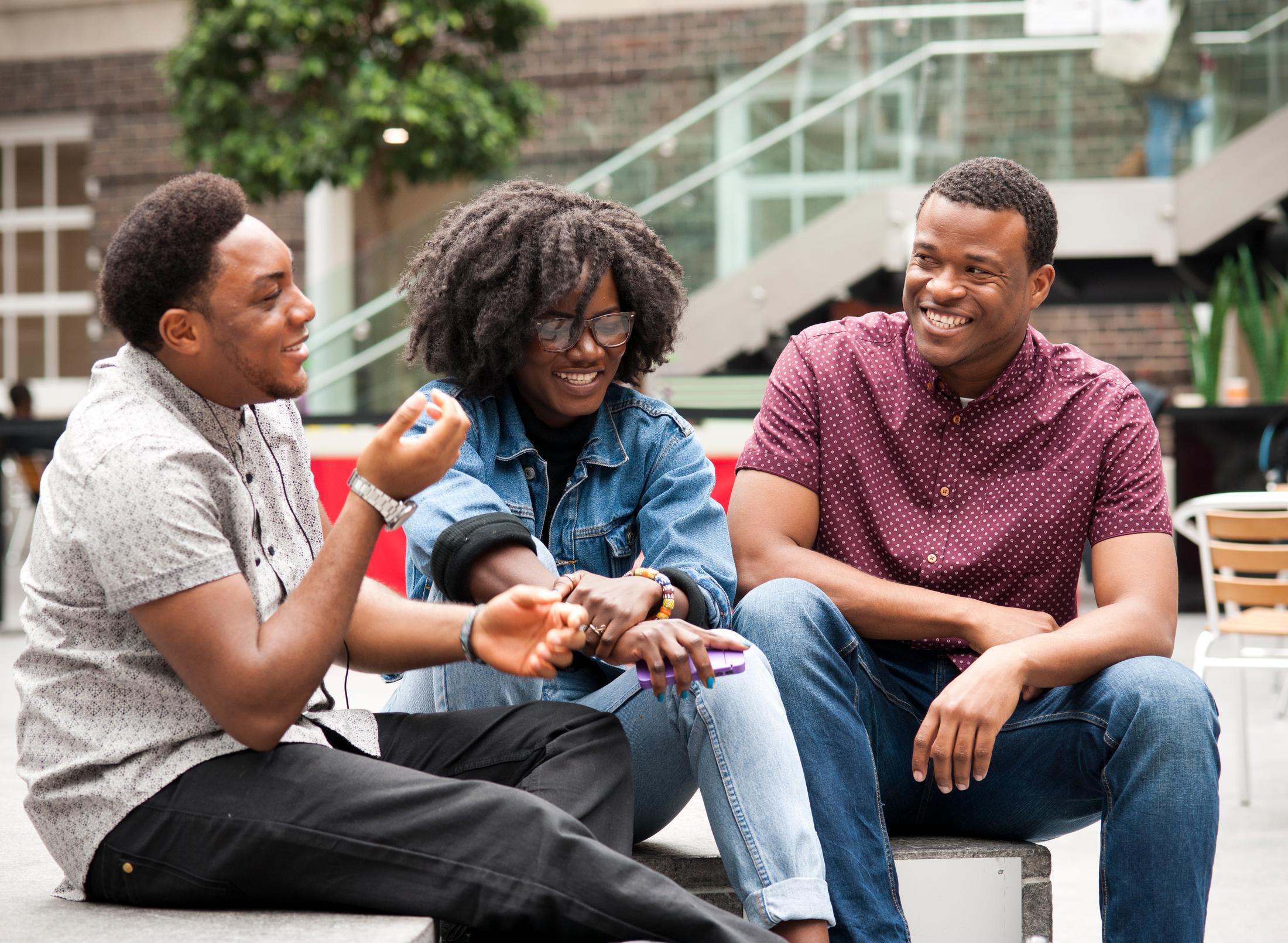 3 students sitting on a courtyard engaged in conversation