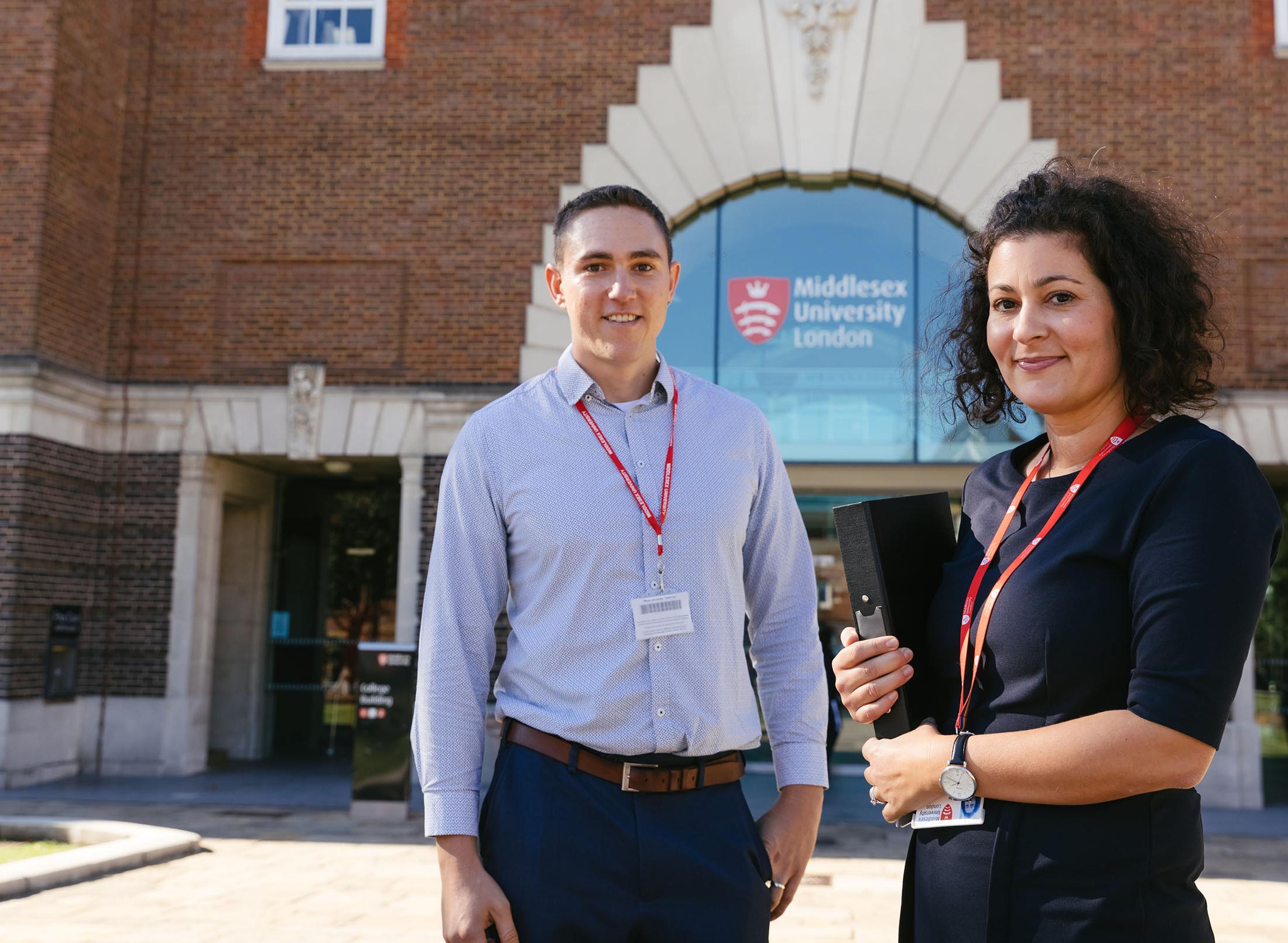 Two friendly staff members pose in front of College Building