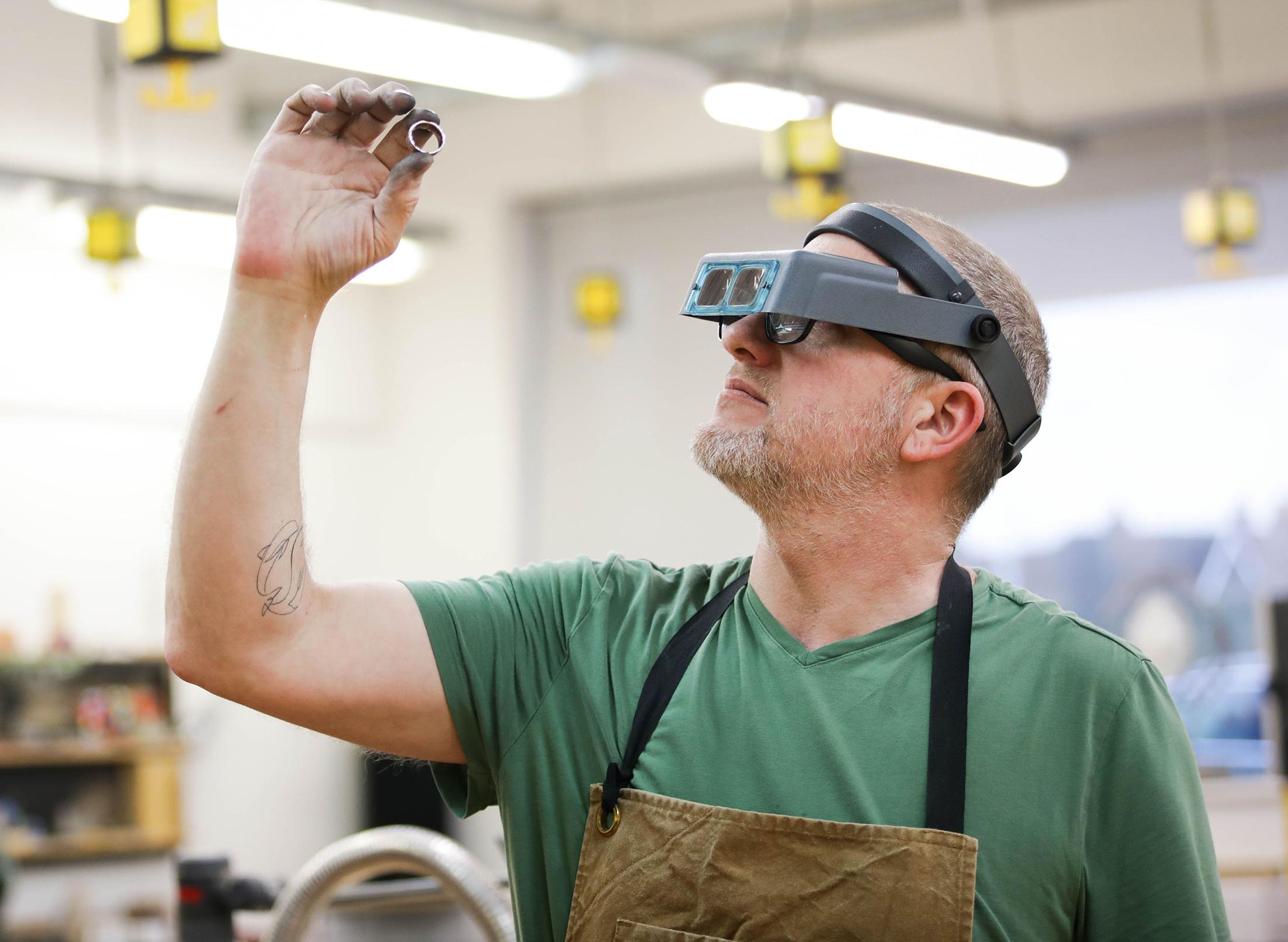 Man in apron and lenses inspects small object