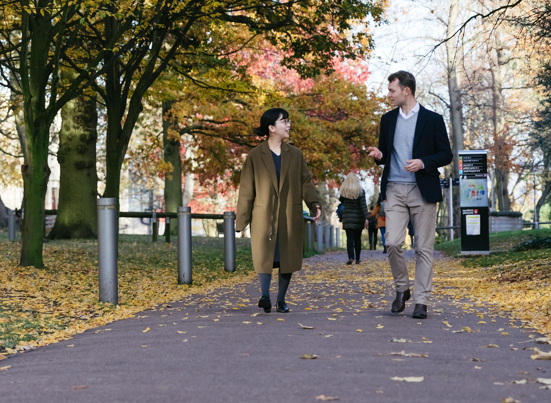 two students walk on campus on tree-lined path in autumn