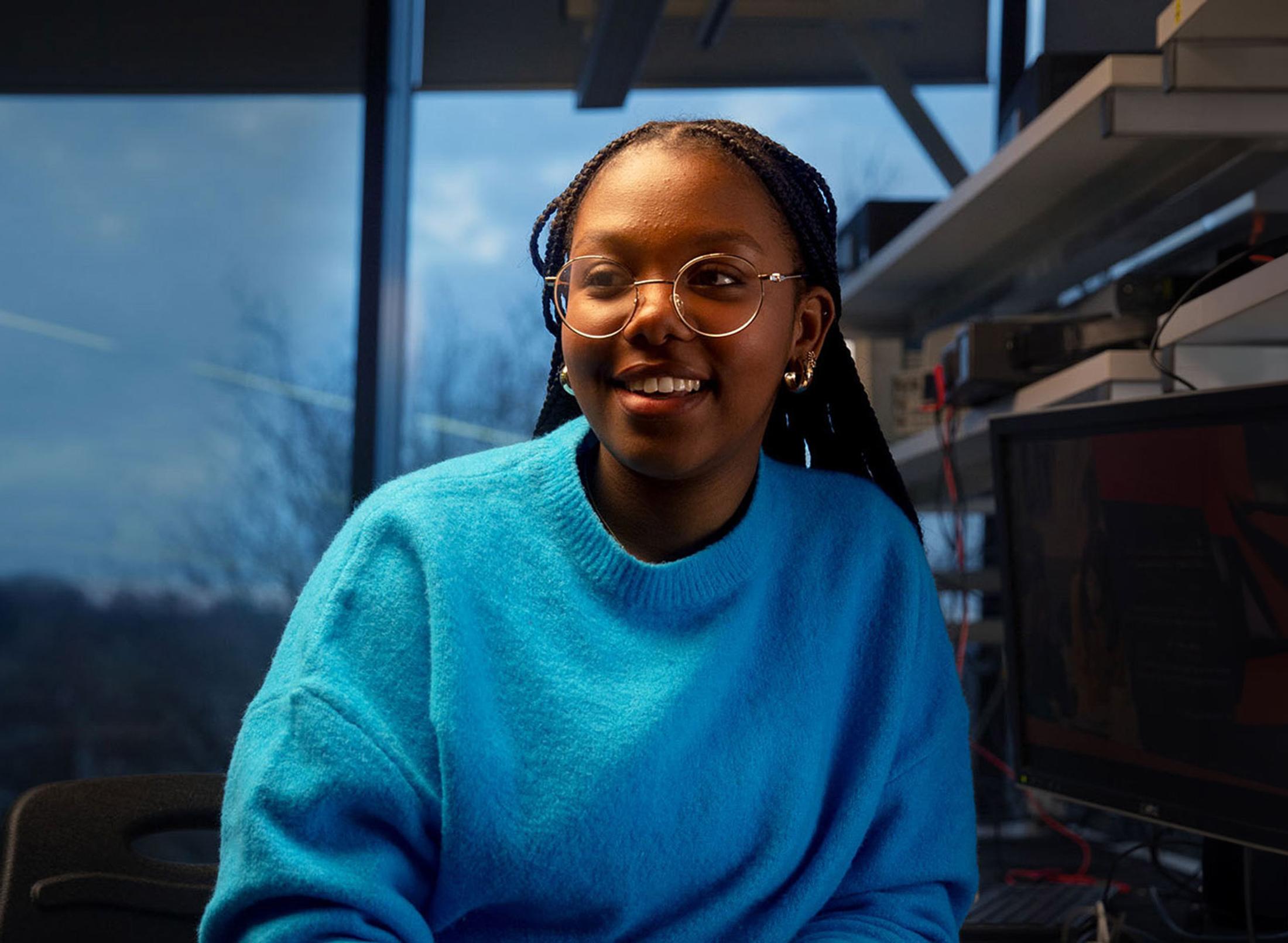 Female student wearing a blue jumper sat in engineering studio