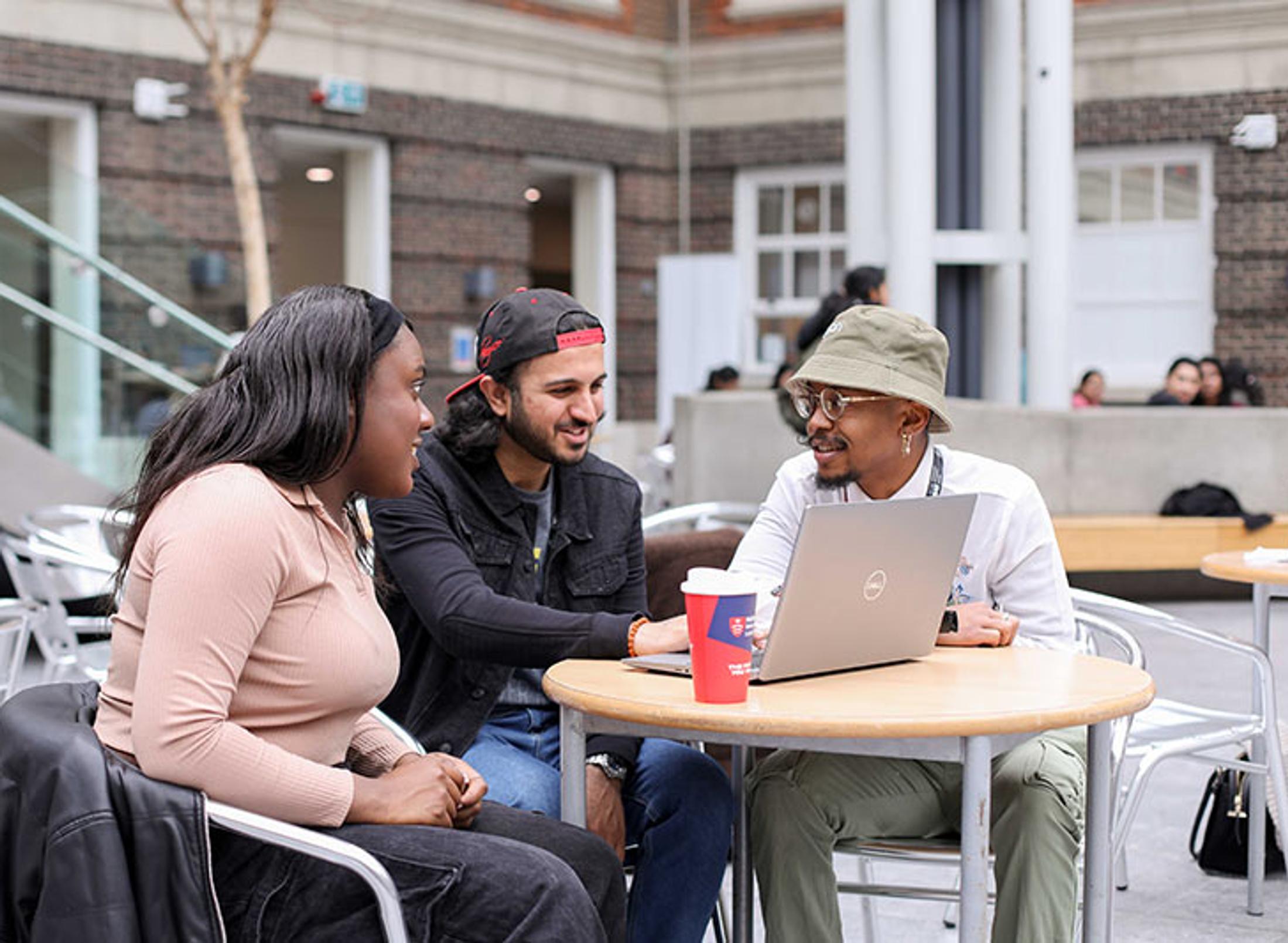 Three students collaborating on a project at a table with a laptop.