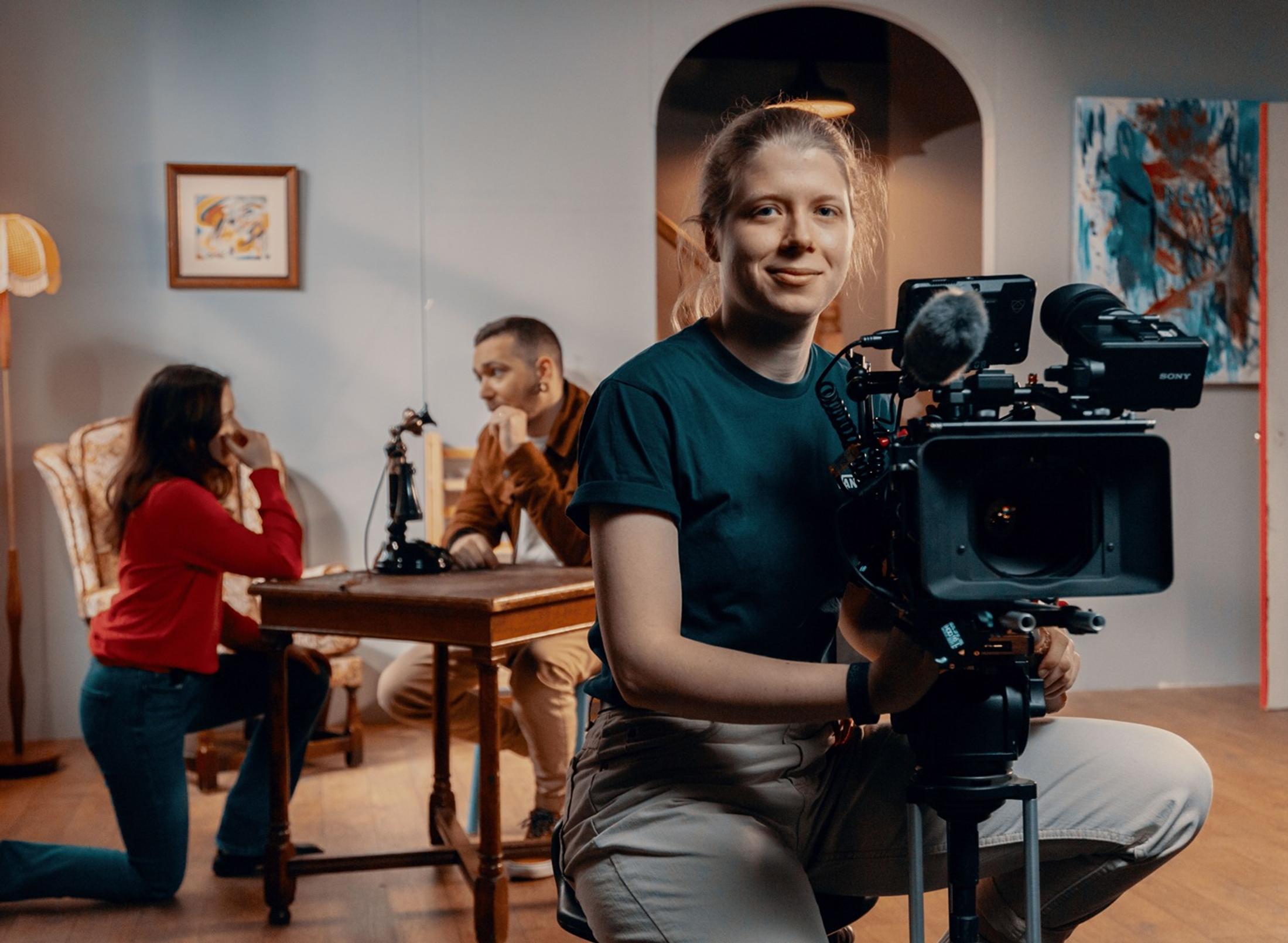 A student using a film camera with two people behind him on set