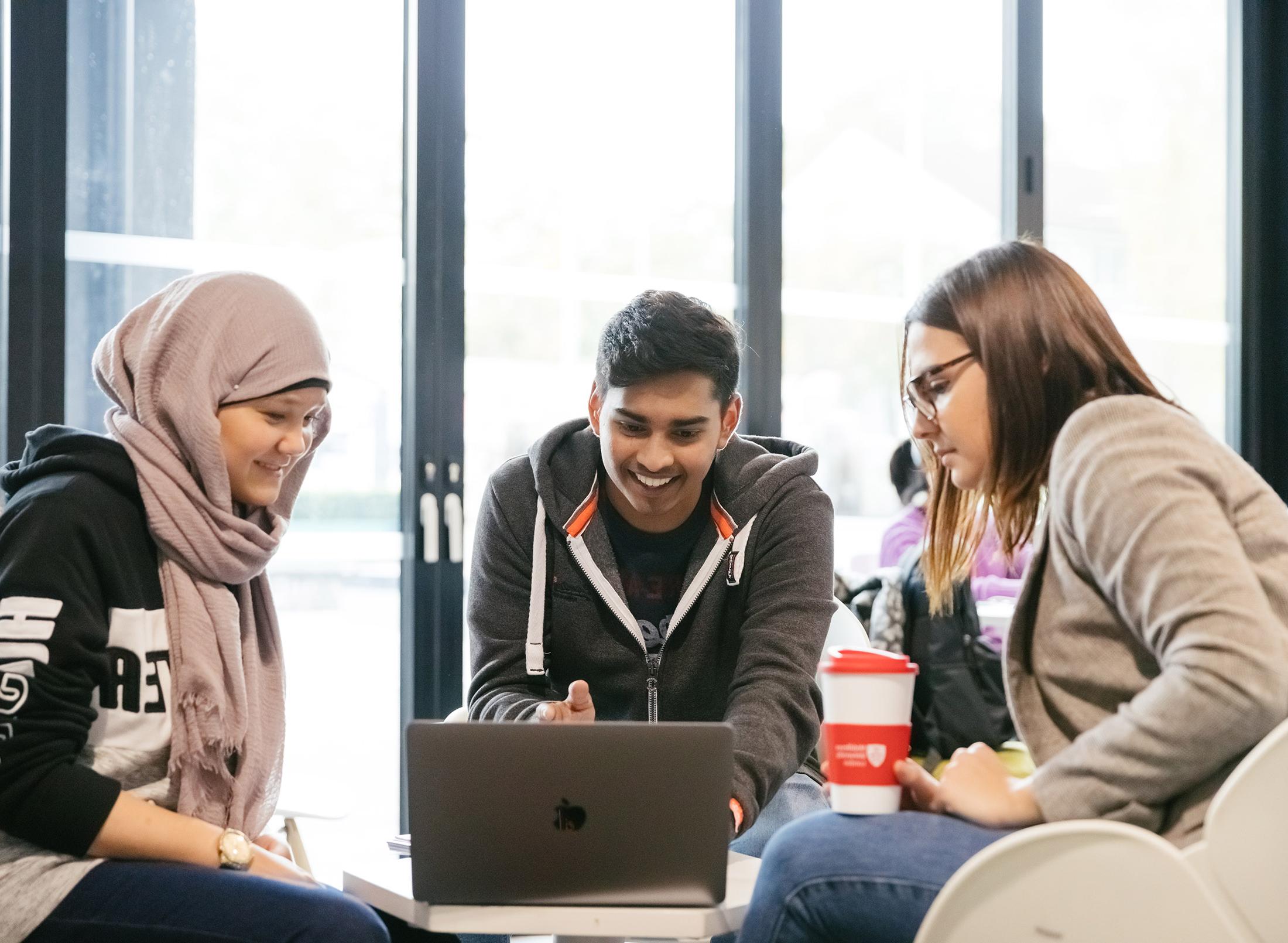three students work informally at laptop