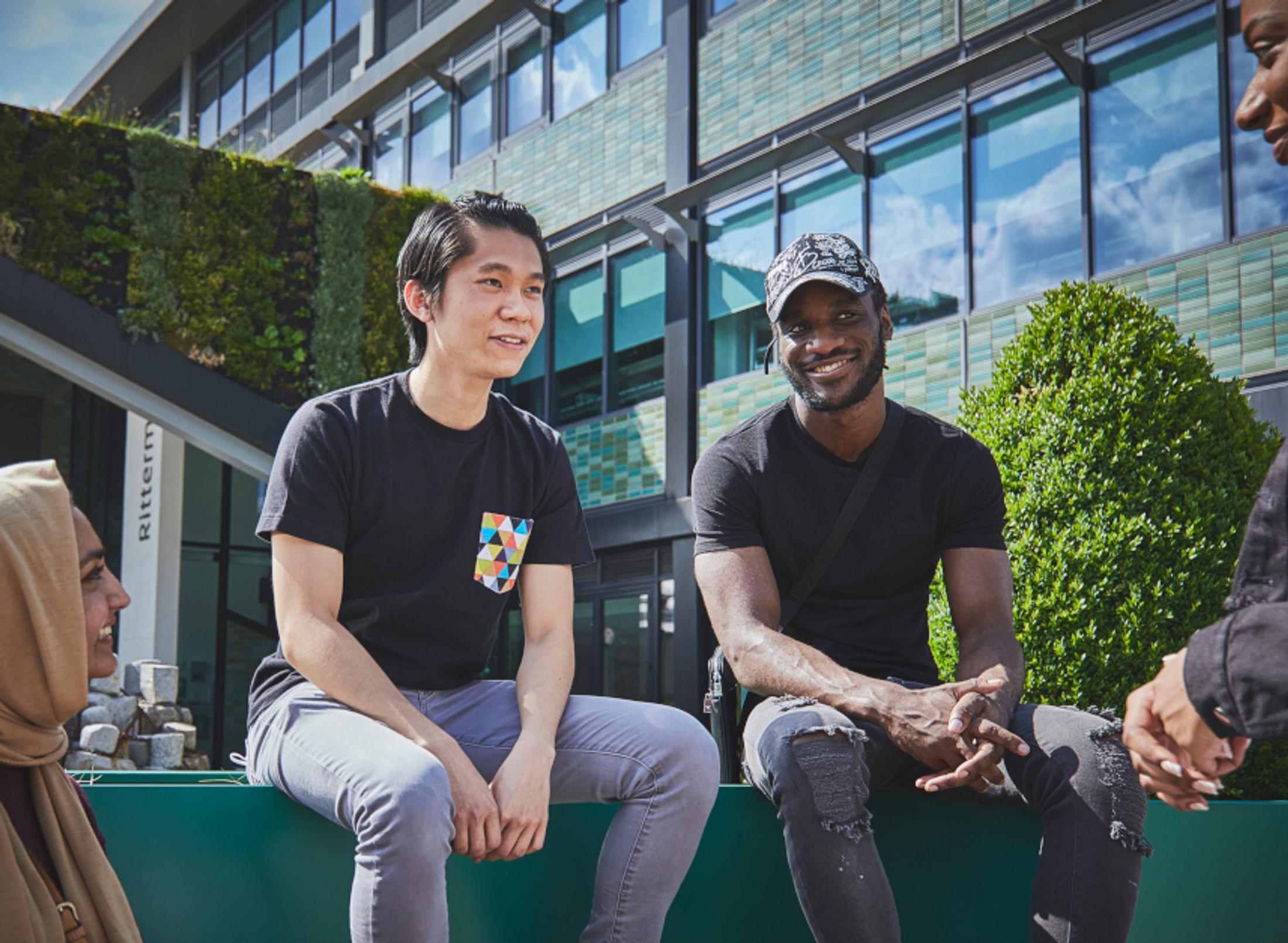 Three young individuals enjoying the outdoors, seated closely on a bench, conversing and smiling.