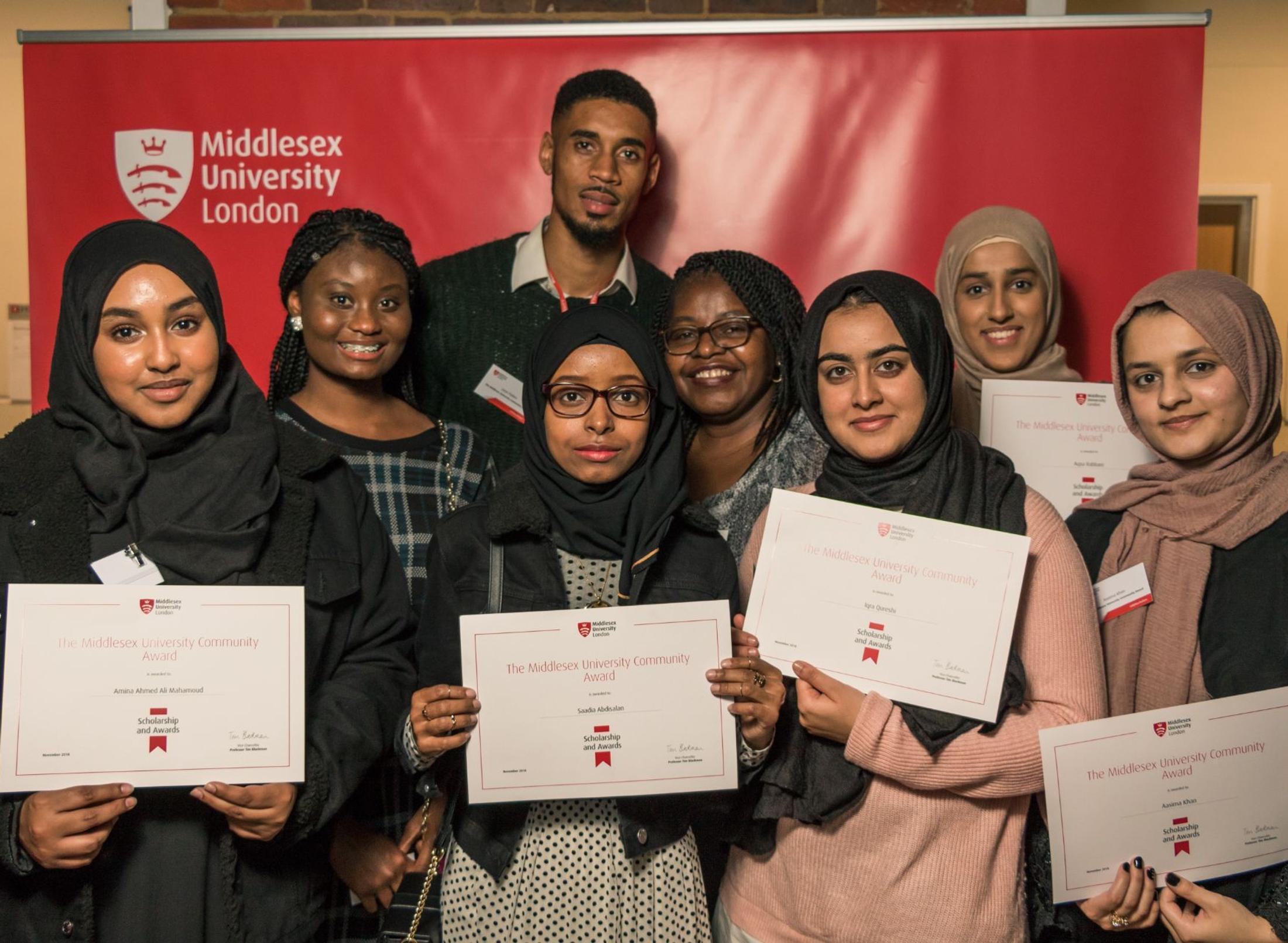 A diverse group of smiling young adults proudly holding up their certificates of achievement.
