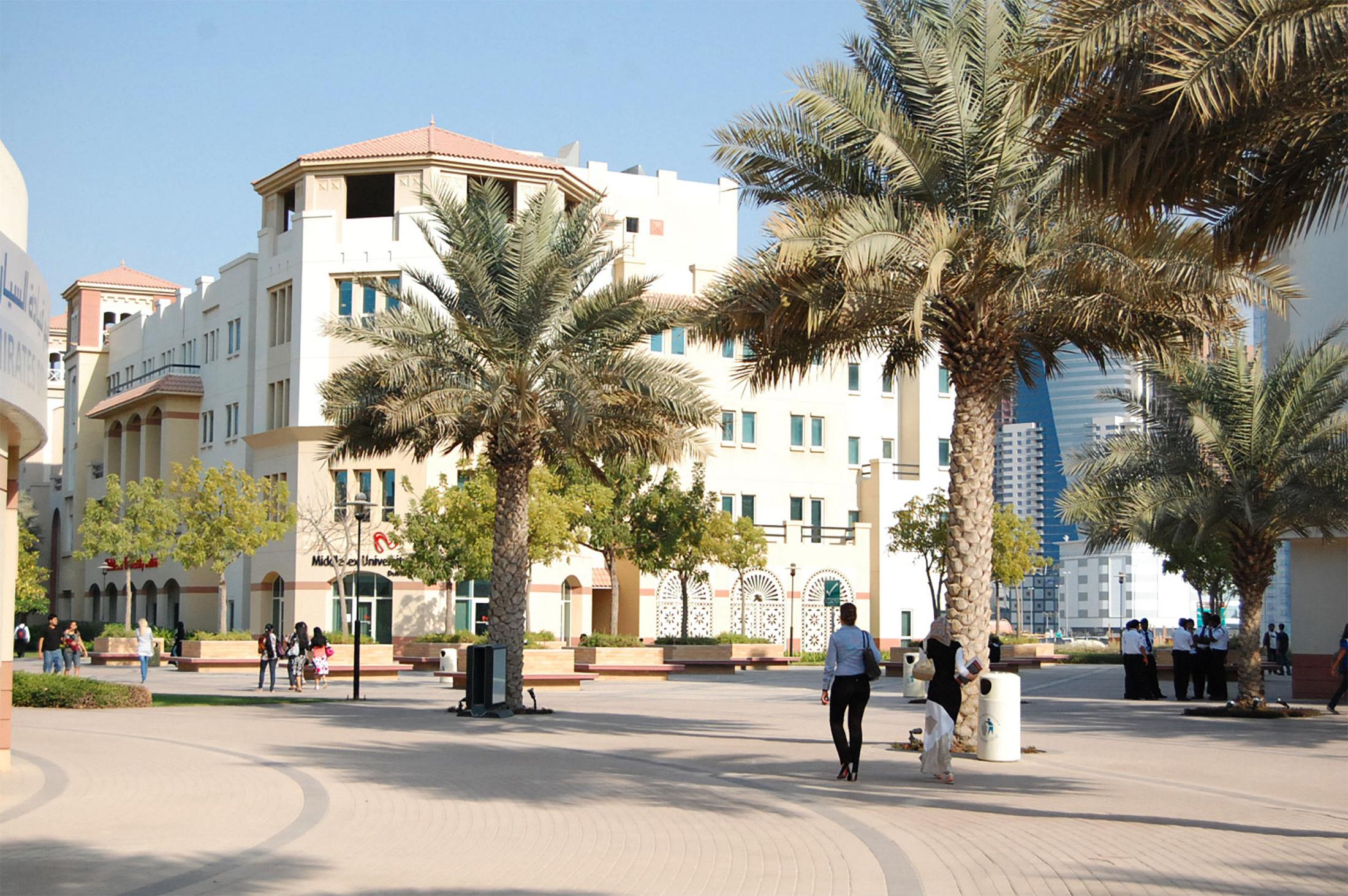 students walking along a street with dubai campus and palm trees in the background