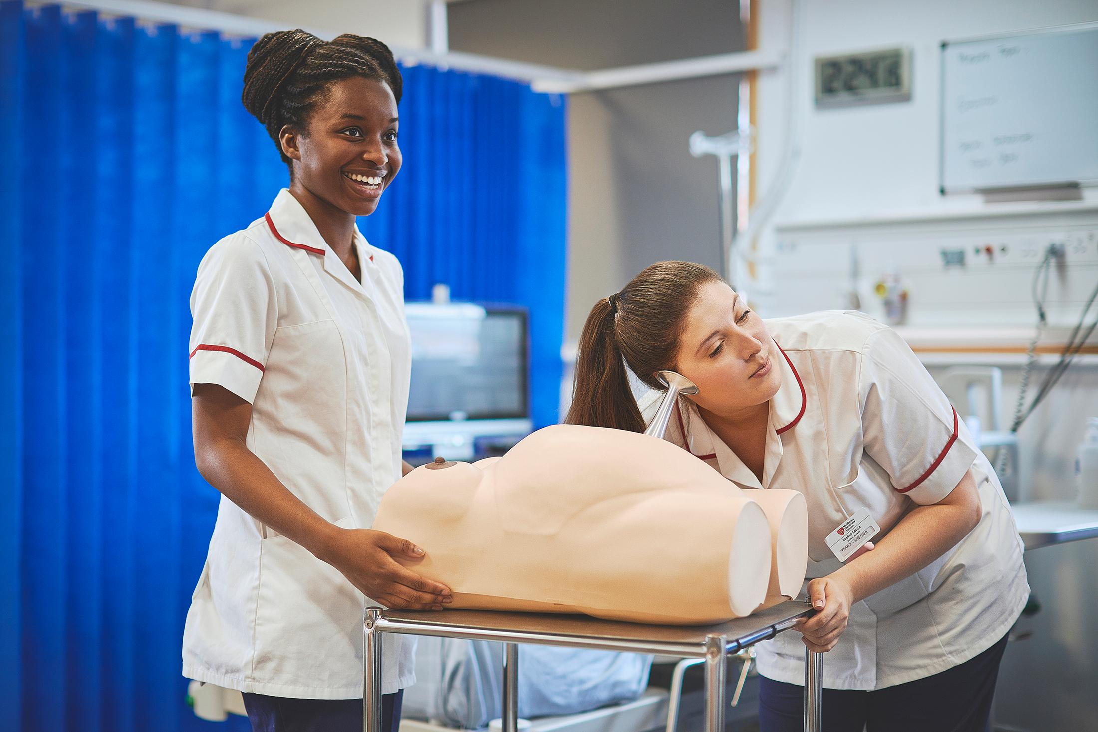 two midwifery students with model of pregnant stomach