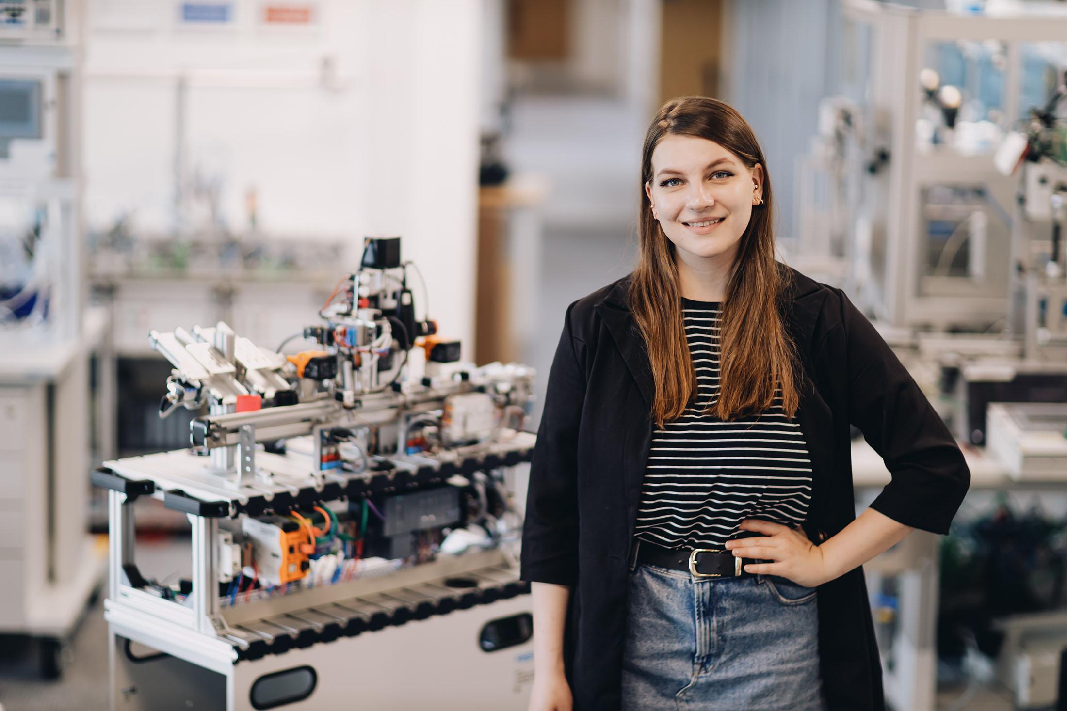 student poses in front of complex machinery