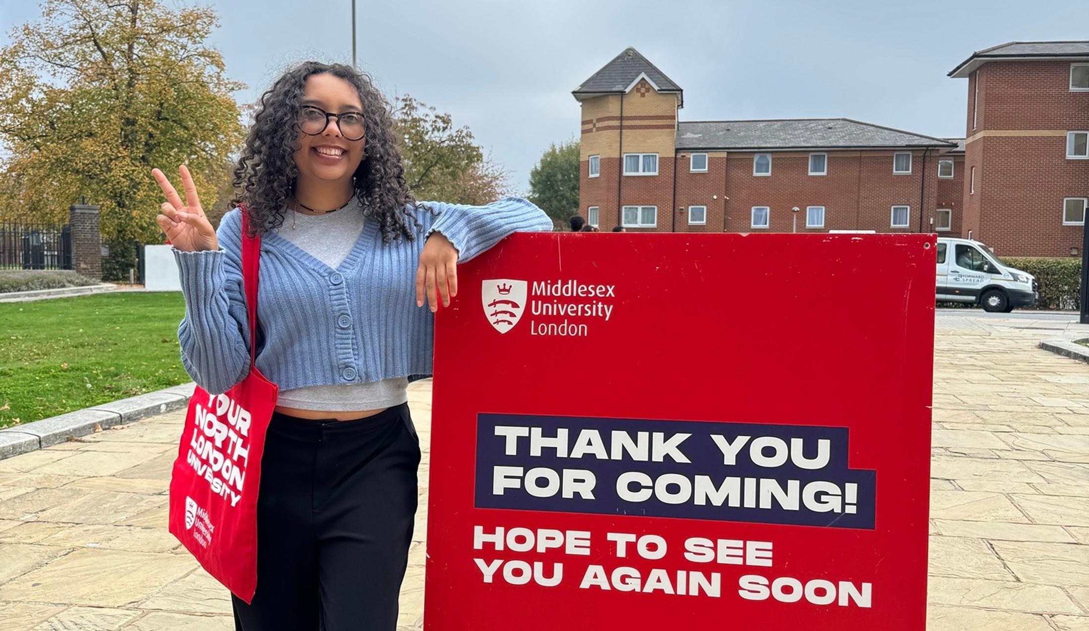 A smiling woman next to a sign which says 