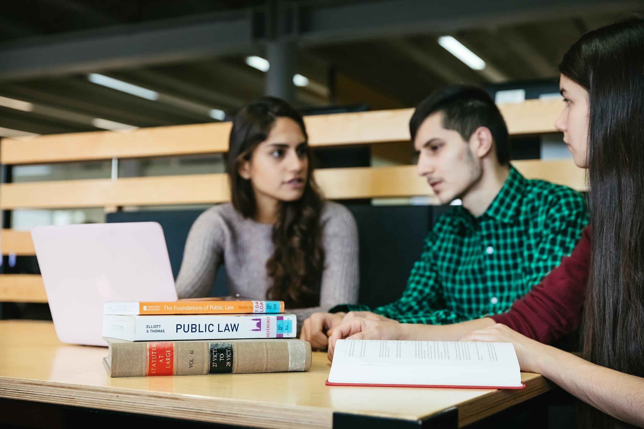 Three law students sat at desk looking at a laptop and books.