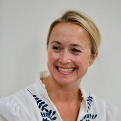 A head and shoulders picture of a smiling woman with blonde hair, wearing a white top
