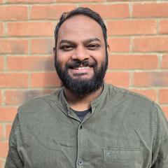 A portrait of Middlesex University graduate Hubert James standing in front of a brick wall