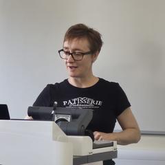 A woman with glasses lecturing at a podium