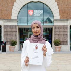 Biomedical Science student standing with her degree certificate outside Middlesex main campus