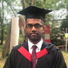 A portrait of a graduate standing in a wooded area wearing an academic cap and gown