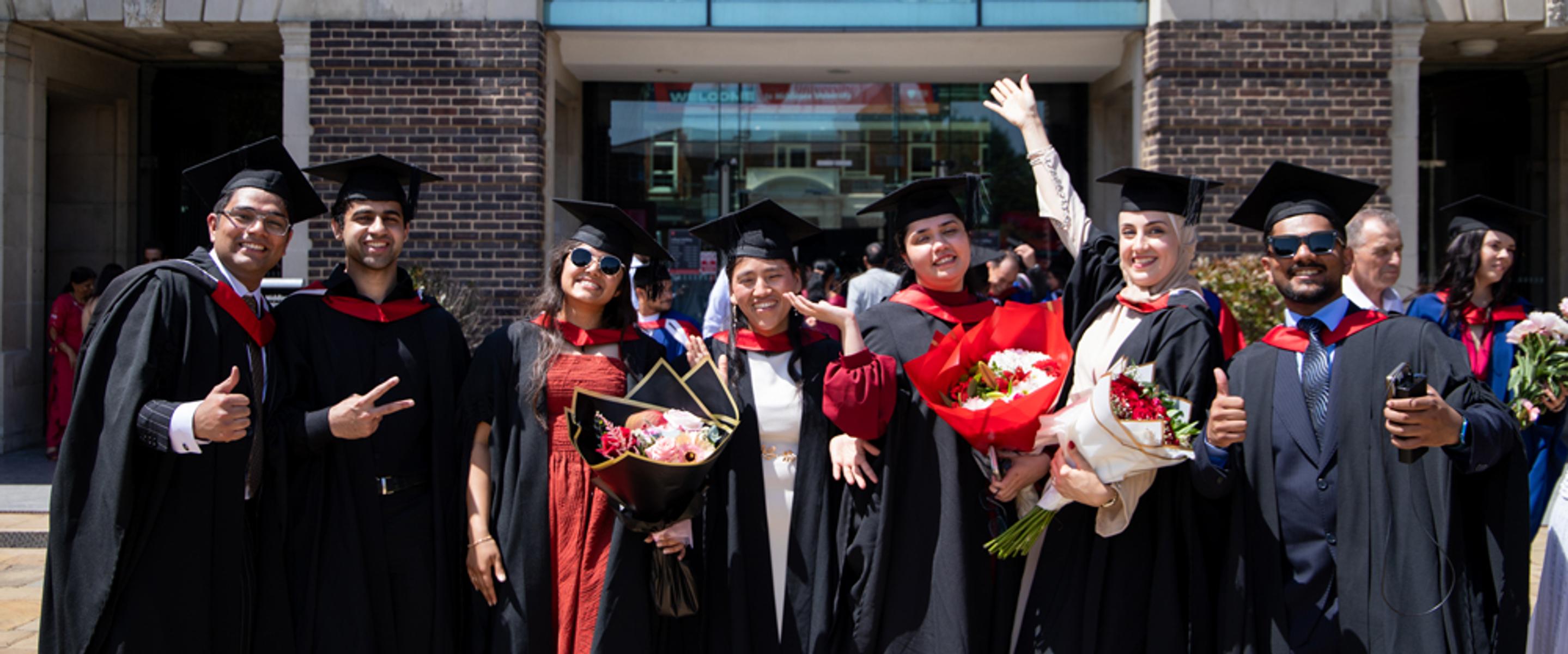 a group of graduates in their academic gowns celebrate attaining  their degrees outside a building
